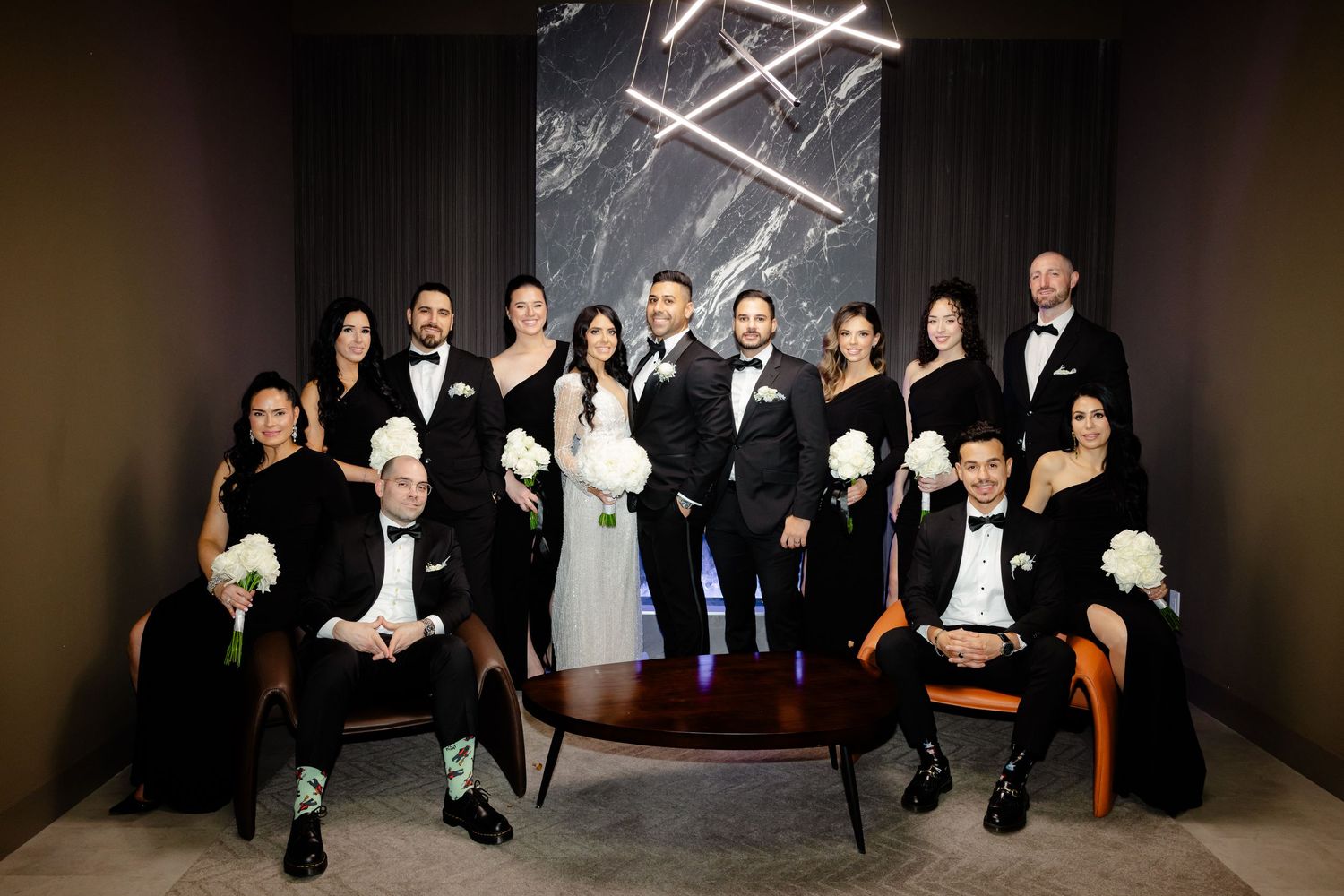 Full wedding party portrait with modern geometric backdrop and dramatic lighting.