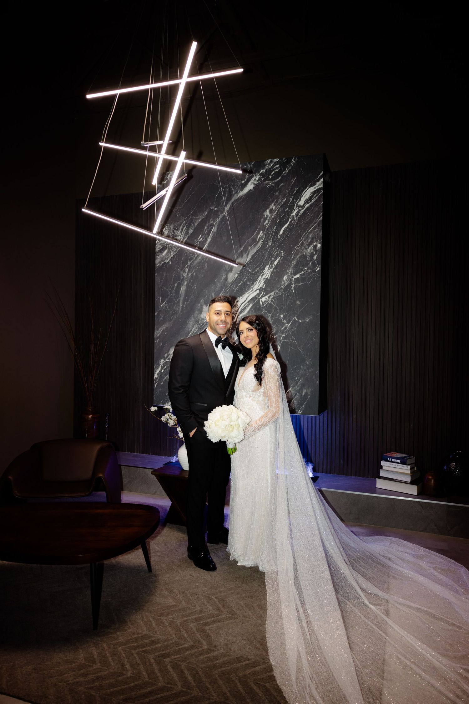 Wedding portrait featuring modern decor with suspended geometric lighting and marble accent wall.