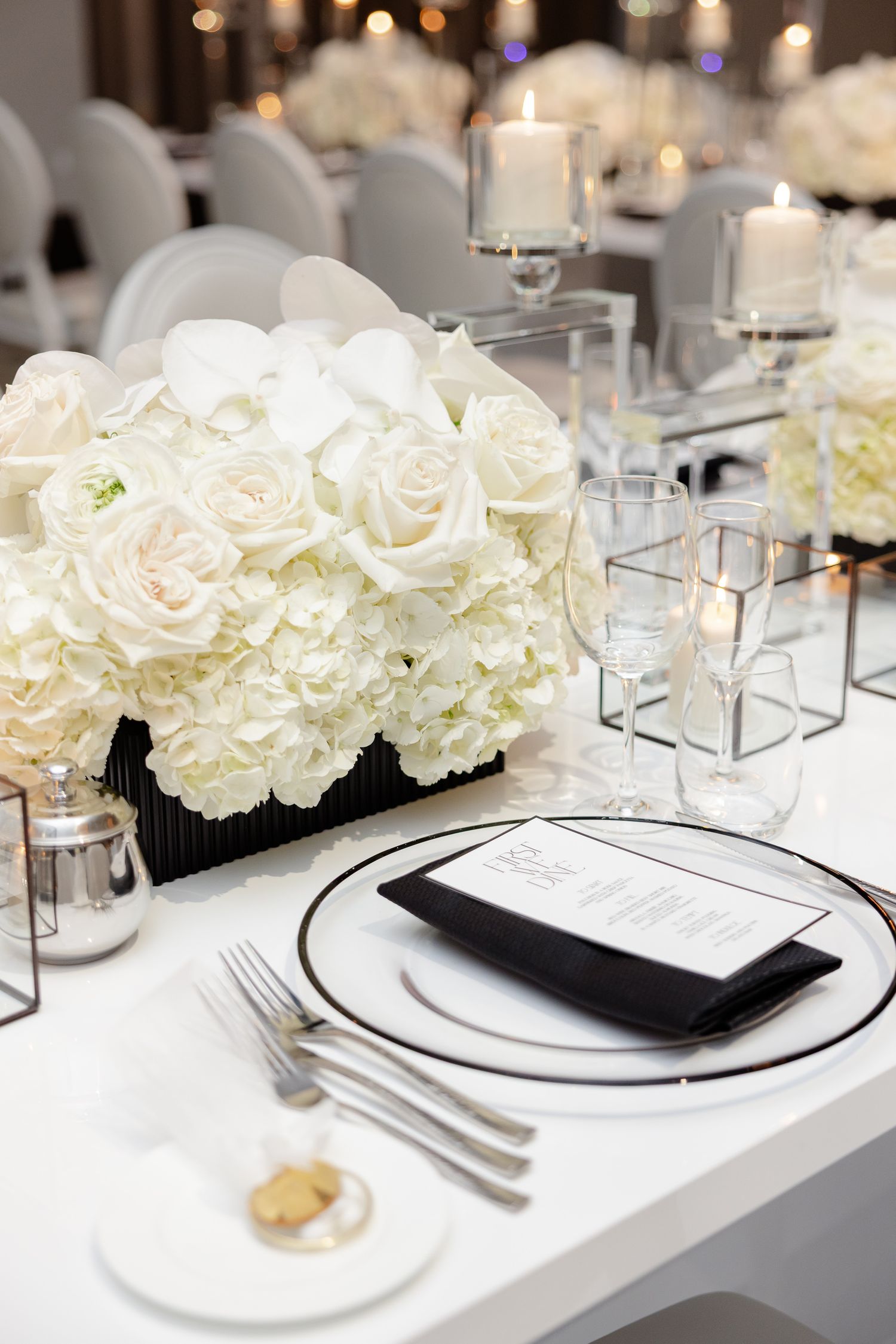 Elegant white wedding table setting with white roses, crystal candleholders, and formal dinnerware on crisp linens.