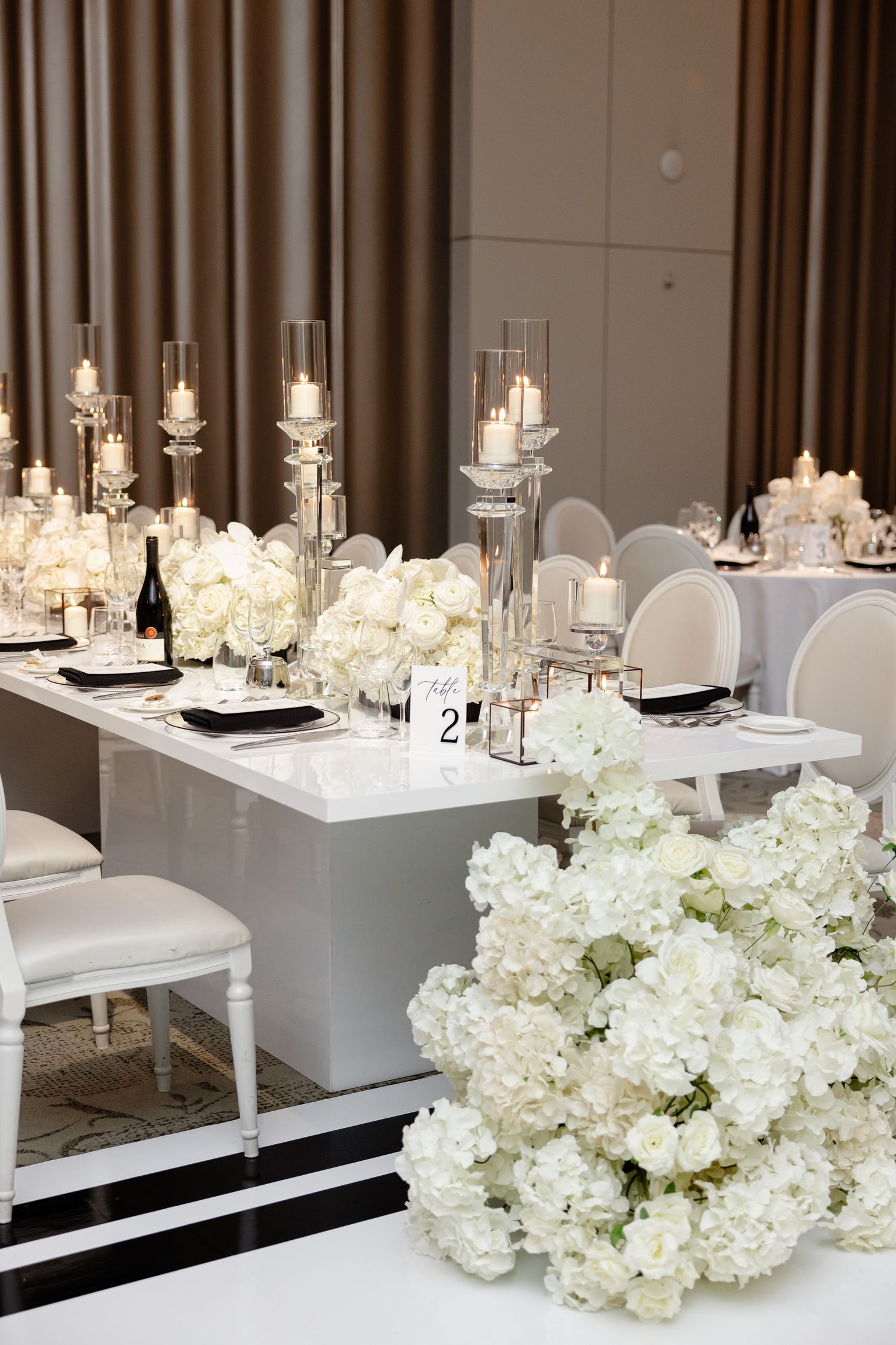 Elegant wedding table settings with white hydrangeas and glowing candles in a modern reception space.