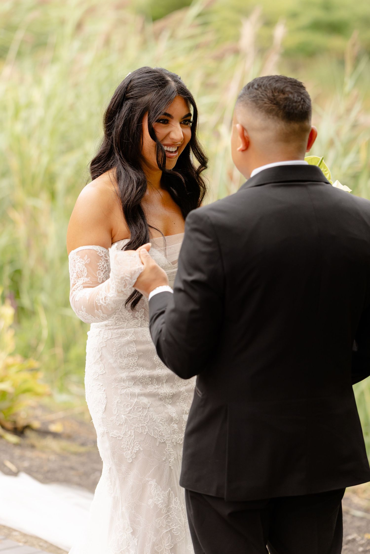A happy couple shares an intimate moment during their wedding ceremony amidst tall grass in nature.