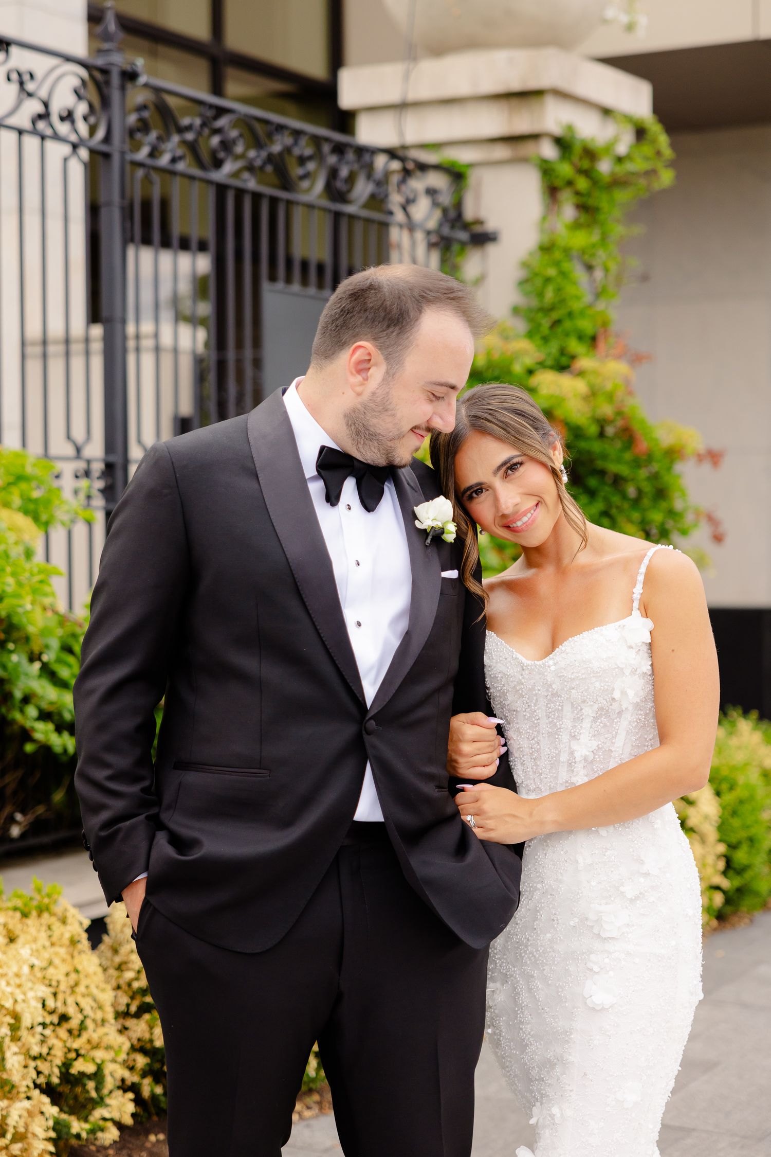 A romantic moment captured in an outdoor garden setting with formal wedding attire and natural light.