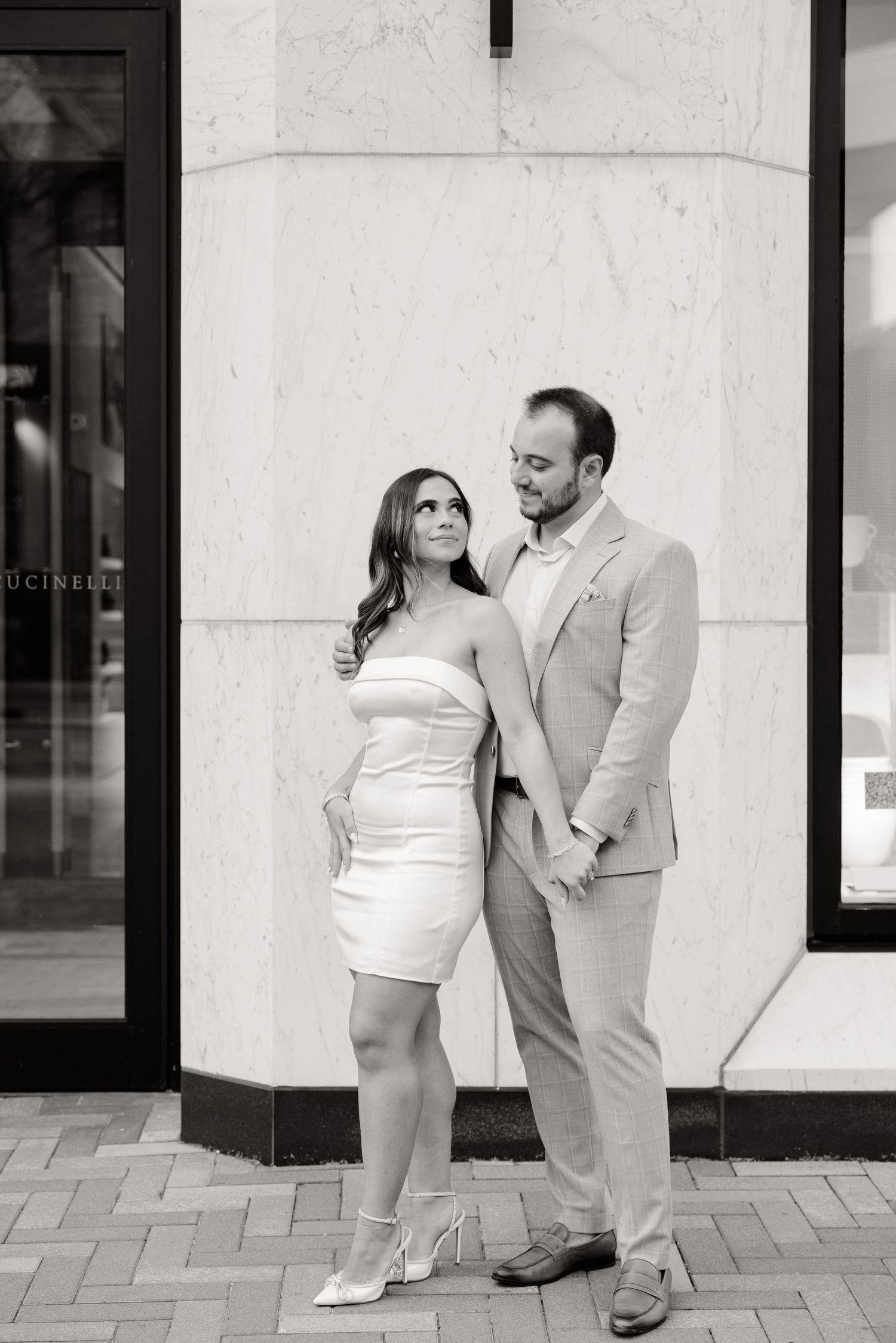 Black and white portrait of couple standing close together against marble wall.