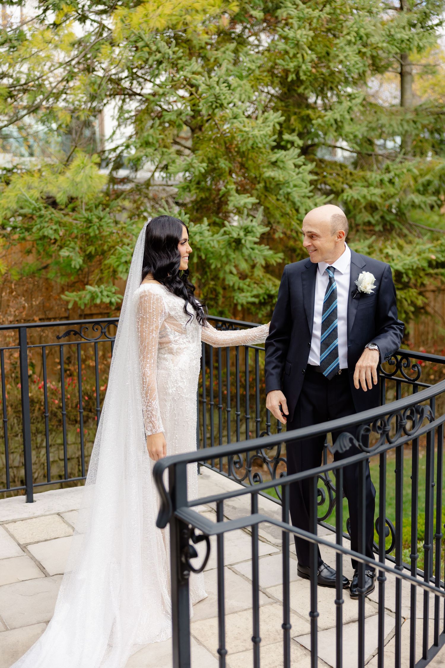 Candid wedding moment captured on elegant stone staircase surrounded by fall foliage.