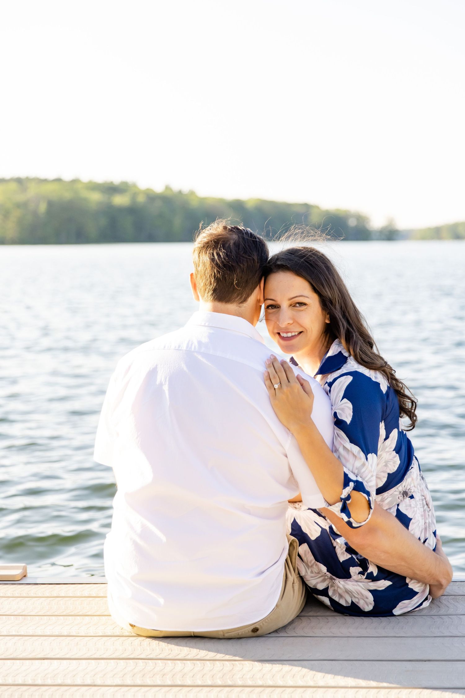 Romantic couple sitting together on wooden dock overlooking serene lake.