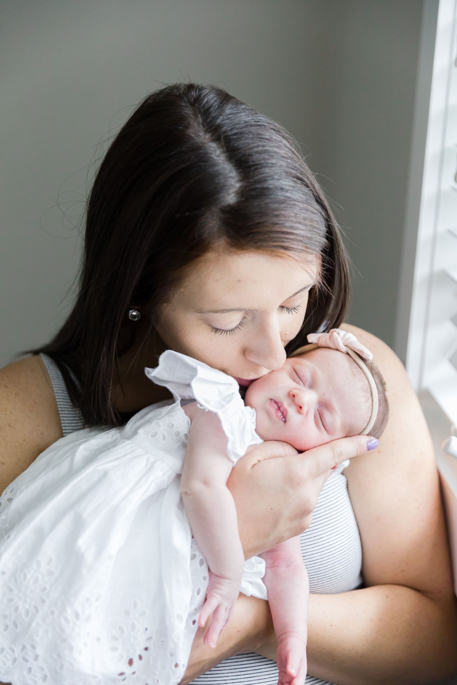 Mother cradling sleeping newborn wearing white lace dress.