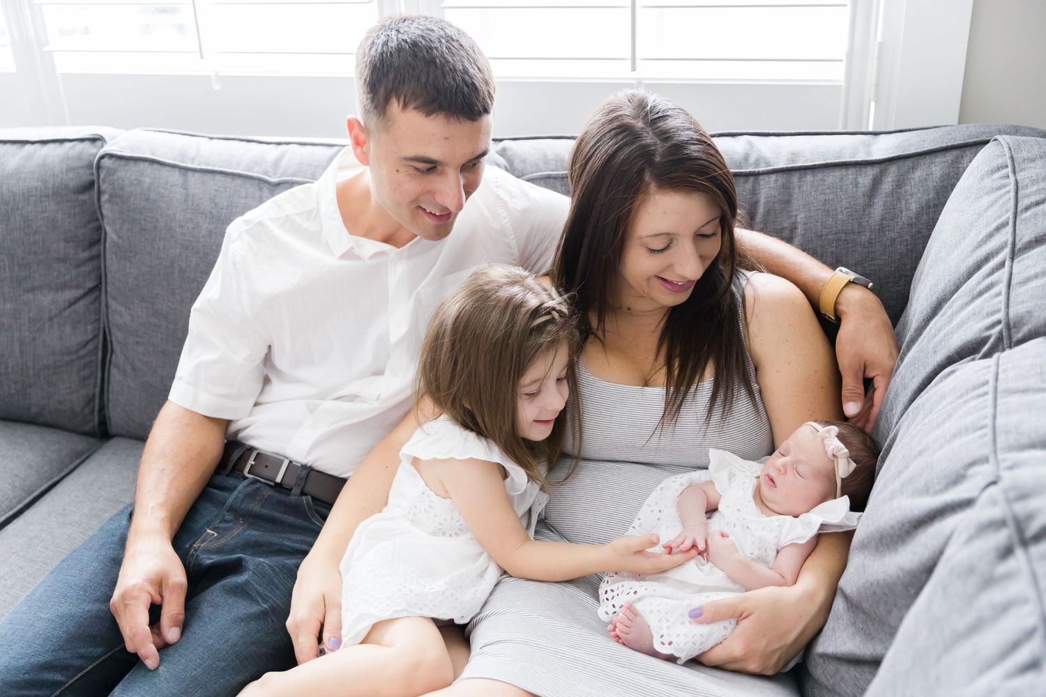 Family gathered on grey couch sharing special moment with newborn.