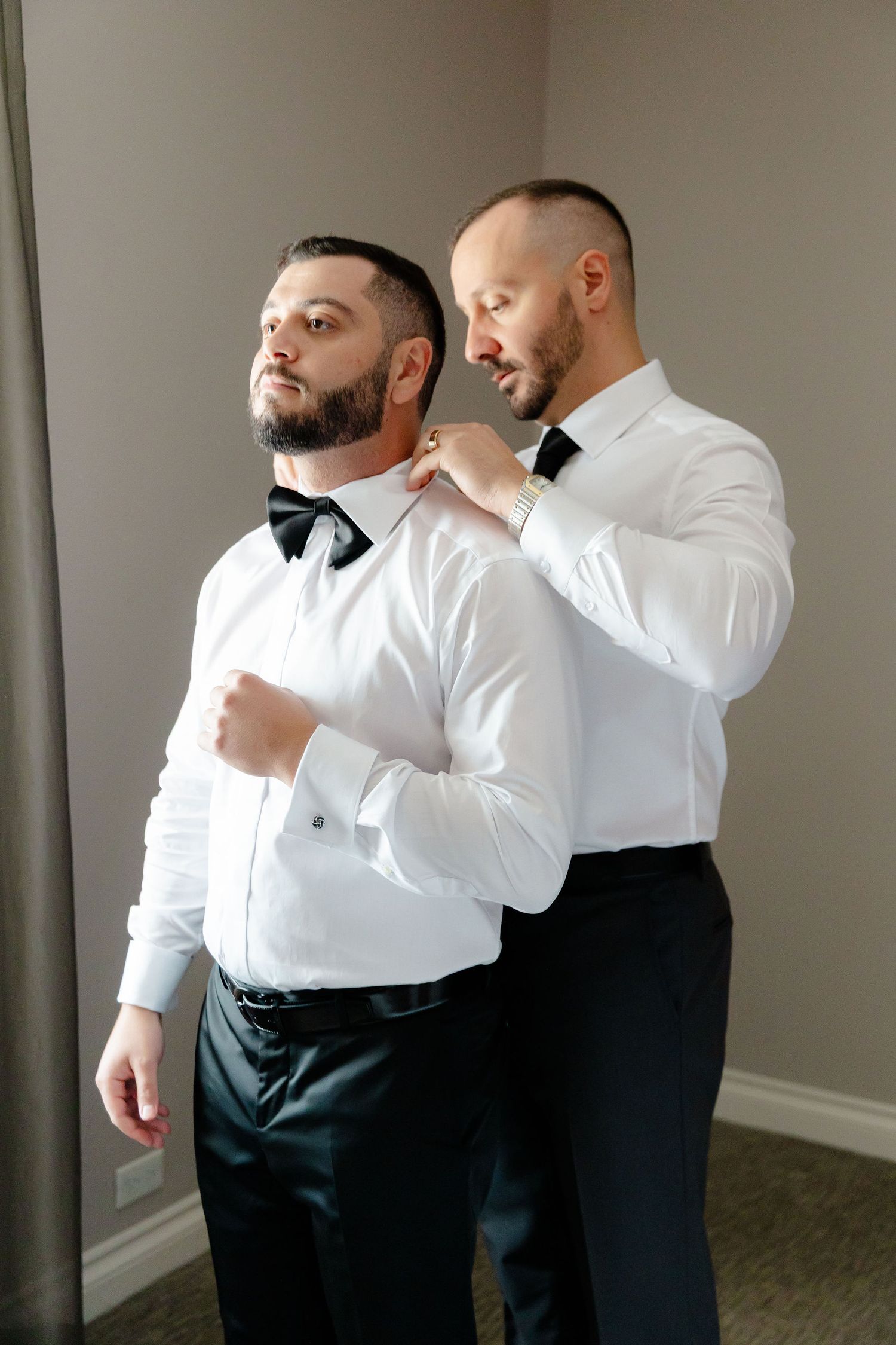 Two people in formal white shirts and black ties share a tender embrace in a minimalist room setting.