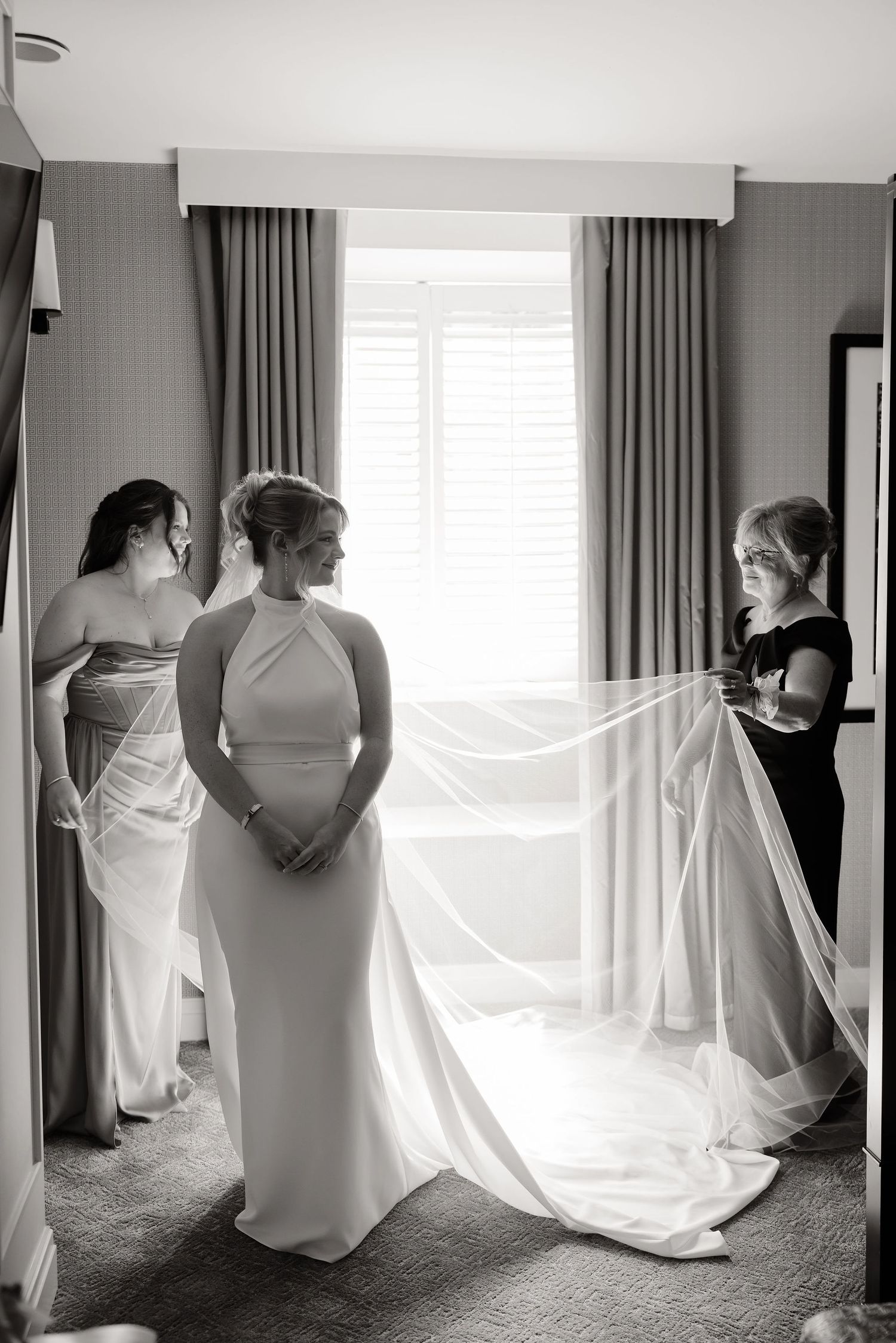 Black and white series showing wedding dress preparations in a bright hotel room.