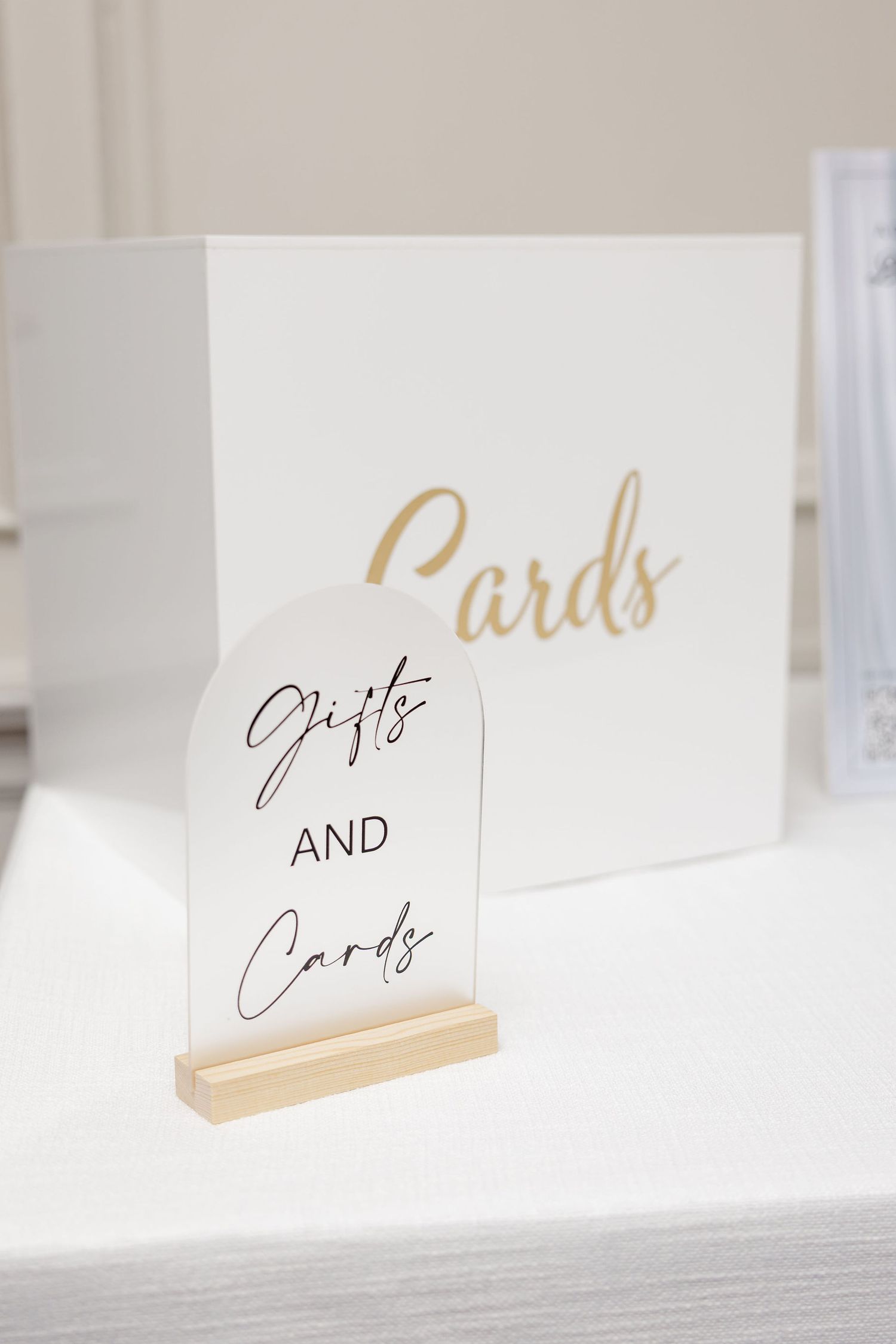 Elegant wedding place cards with gold calligraphy text displayed on wooden holders against a white surface.