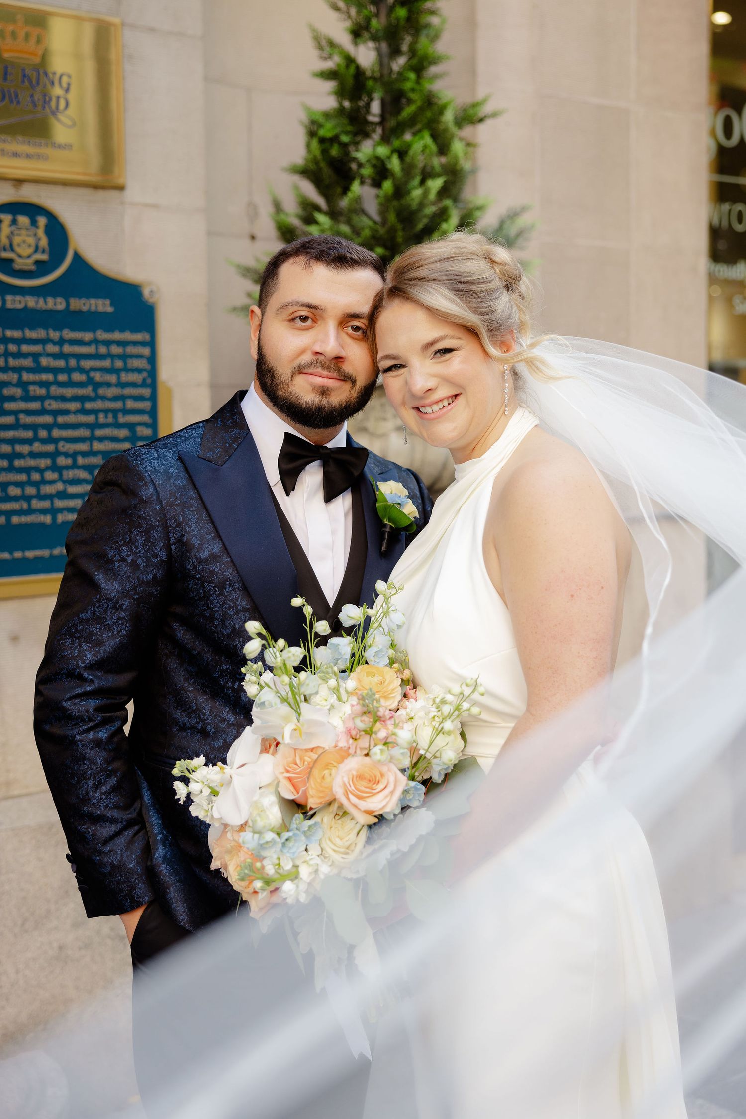 Romantic wedding portrait with flowing white veil and peach floral bouquet.