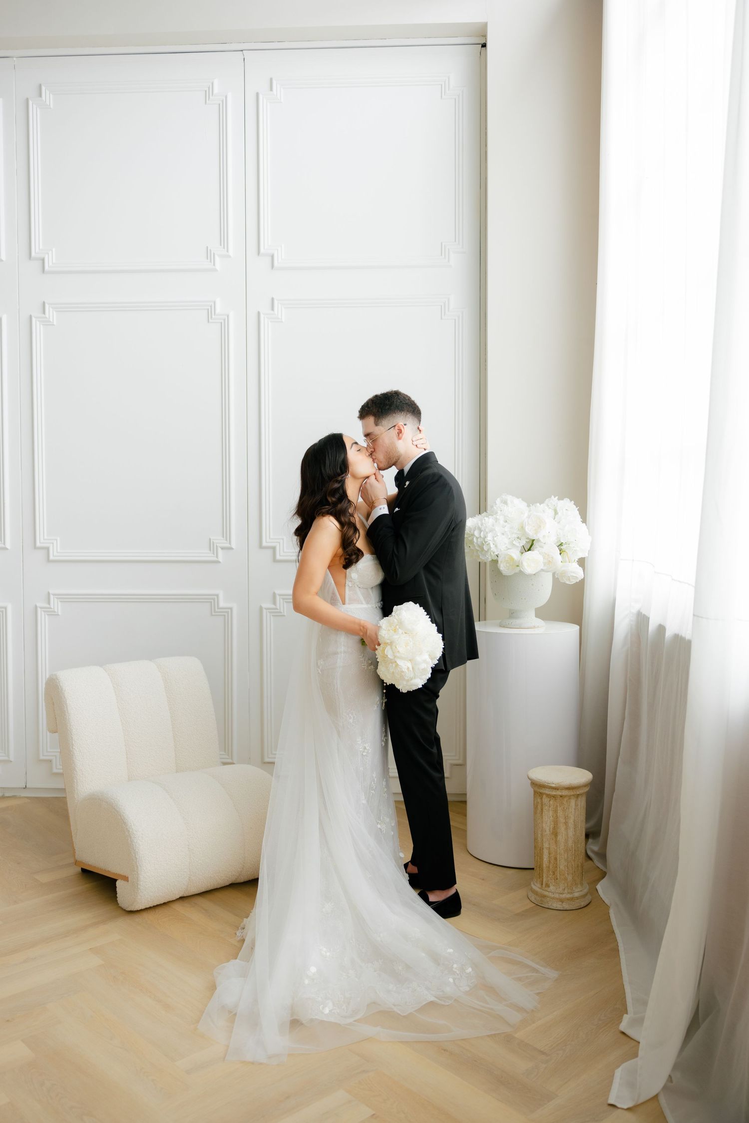 A romantic wedding photo showing a couple's tender embrace in an elegant white room setting.