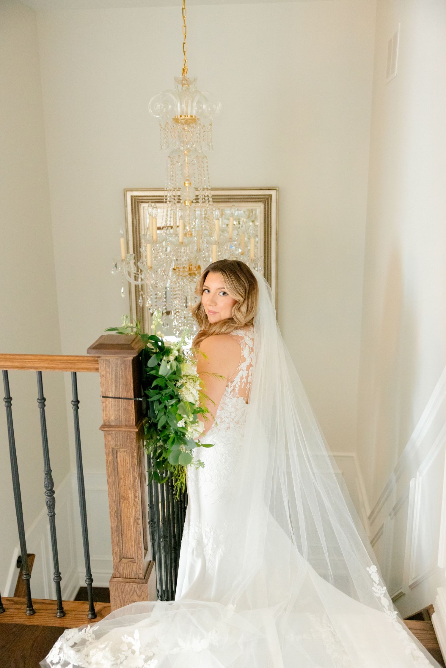 Elegant bridal portrait on staircase featuring flowing veil and cascading greenery bouquet.