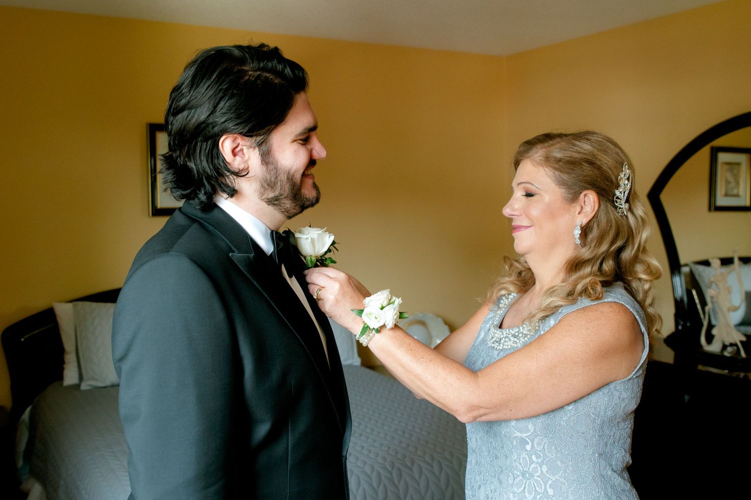 Woman in blue dress helping adjust boutonniere on man's tuxedo lapel.