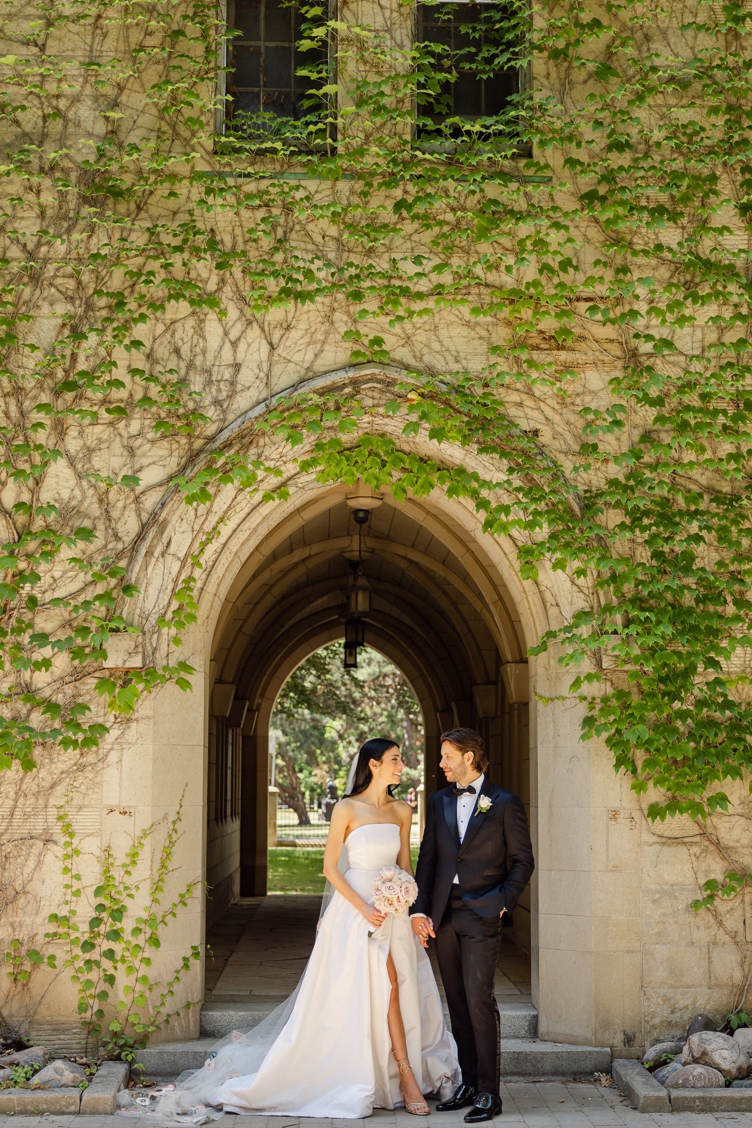 Couple stands in stone archway covered with green ivy vines.
