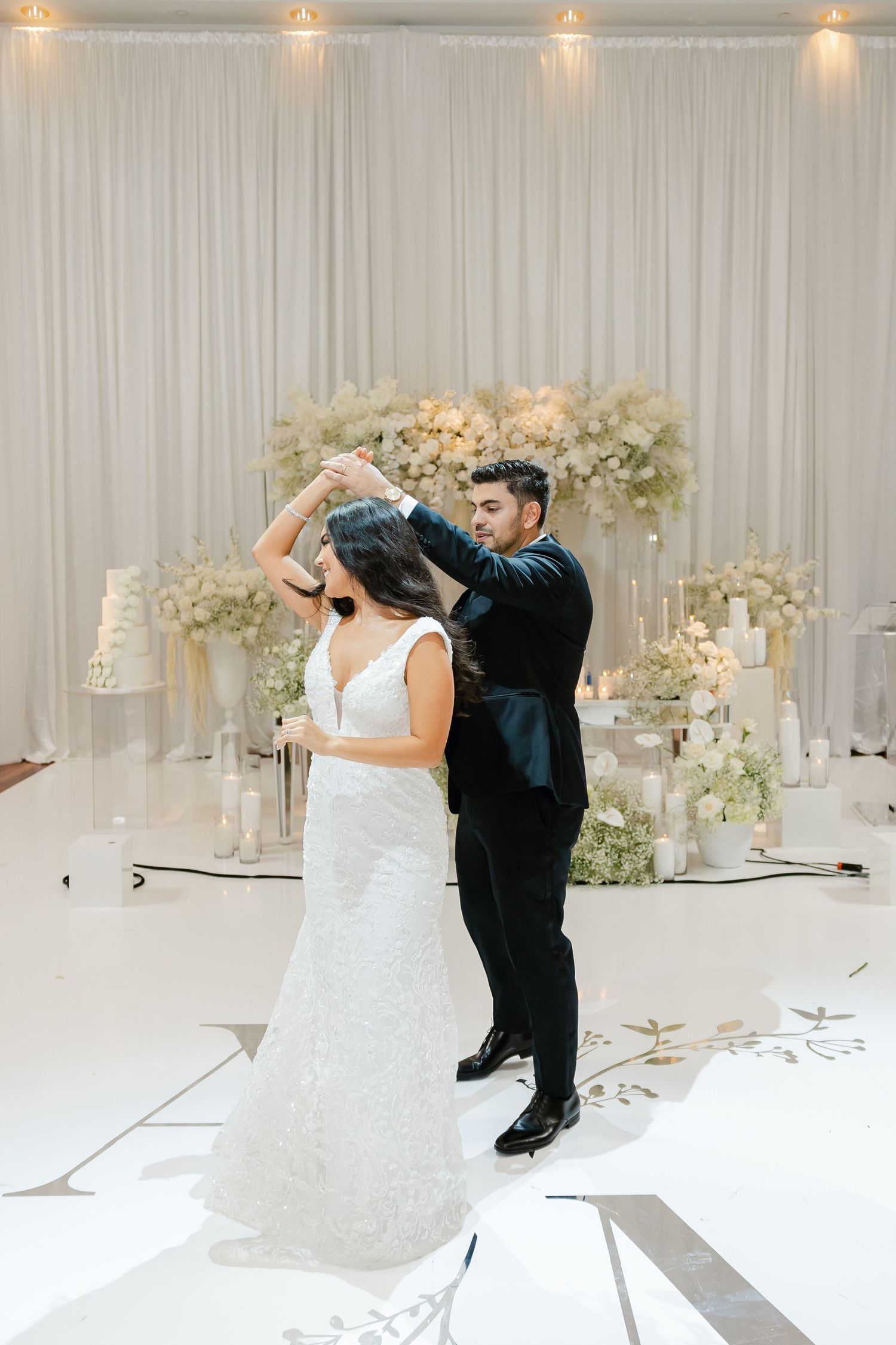 A couple performs an elegant dance move during their wedding reception with floral decor.