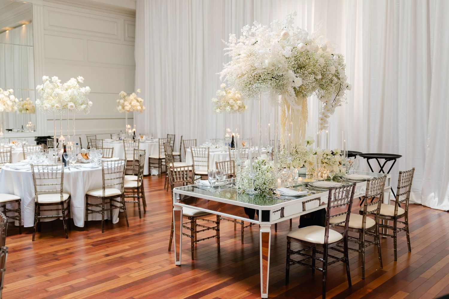 Modern wedding reception setup with mirrored tables and white floral arrangements in an elegant venue.