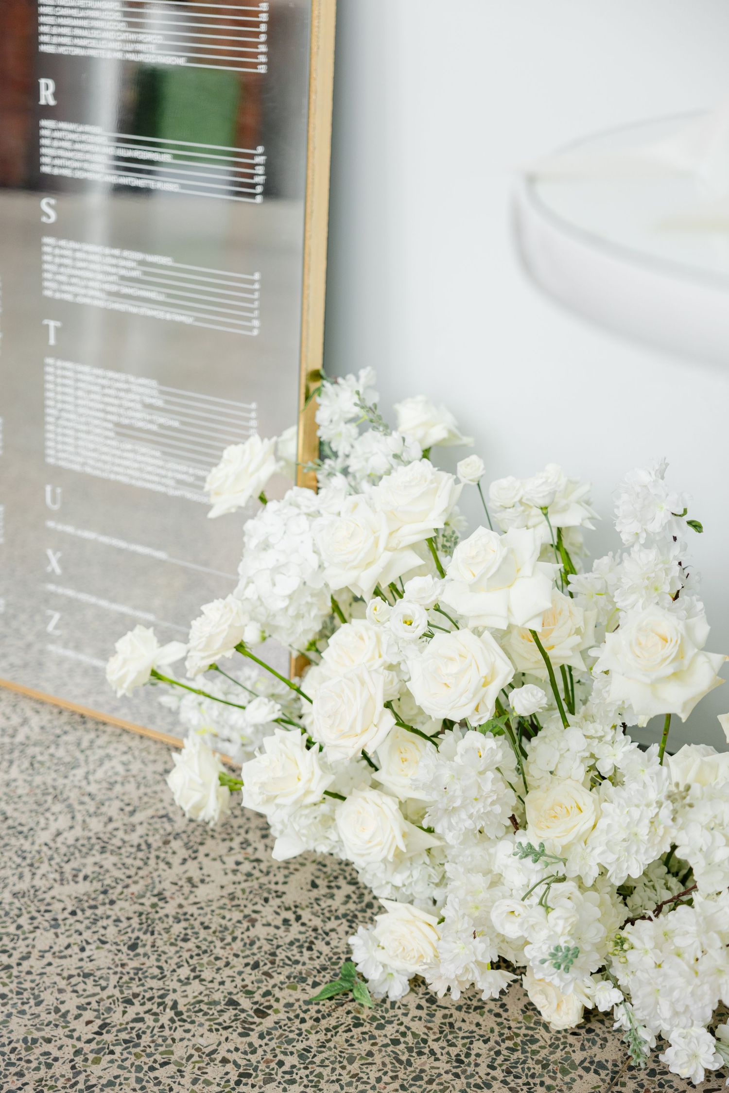 Fresh white roses and carnations arranged beside mirrored surface with text display.