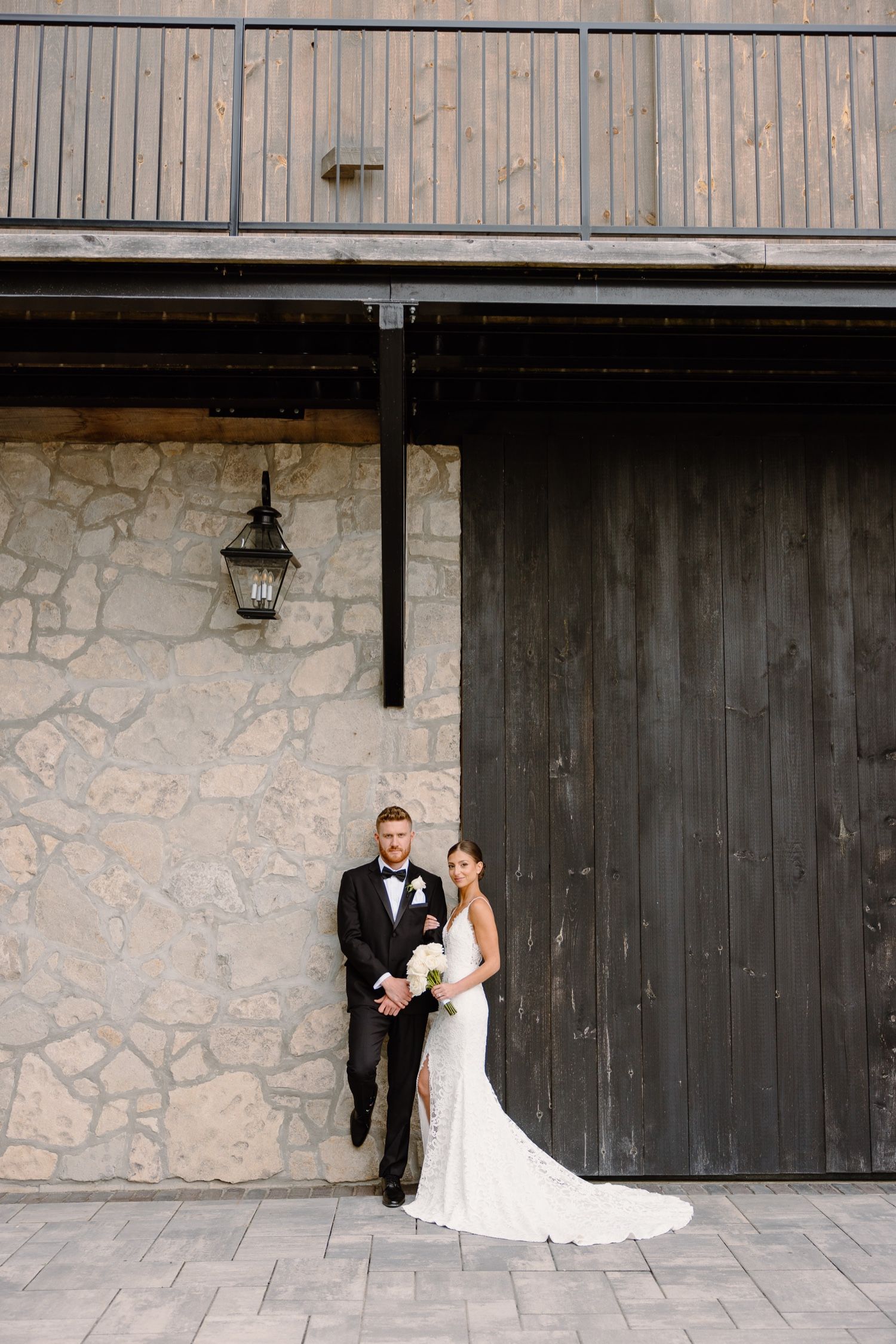 Elegant wedding photo against rustic stone wall and dark wooden door with vintage lantern.