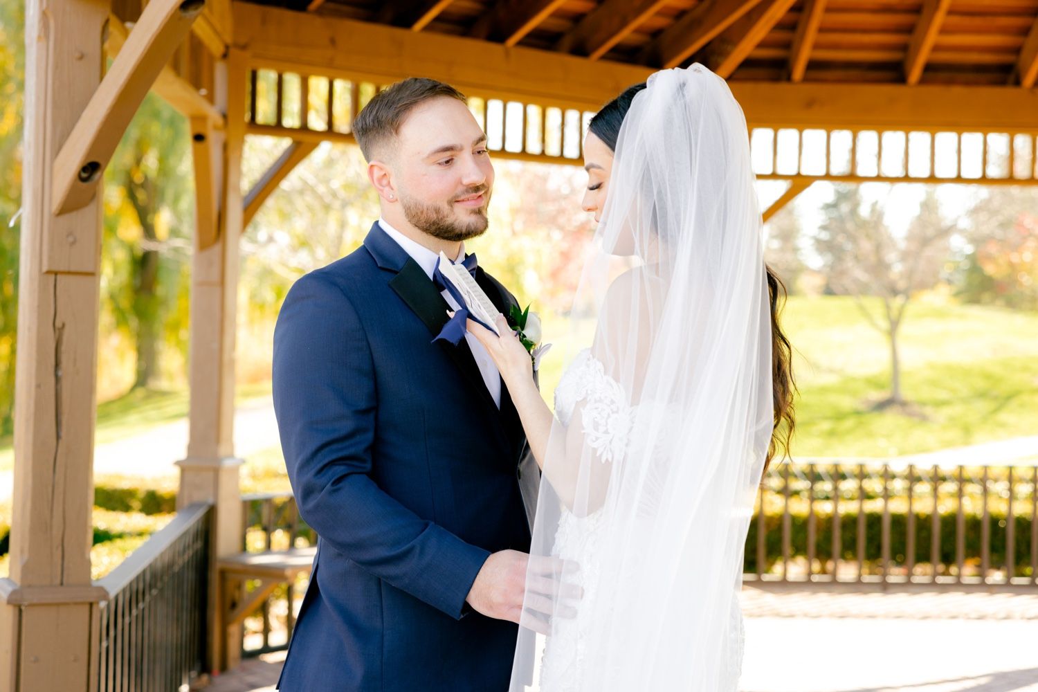 Newlywed couple shares a tender moment under a wooden gazebo on their wedding day.