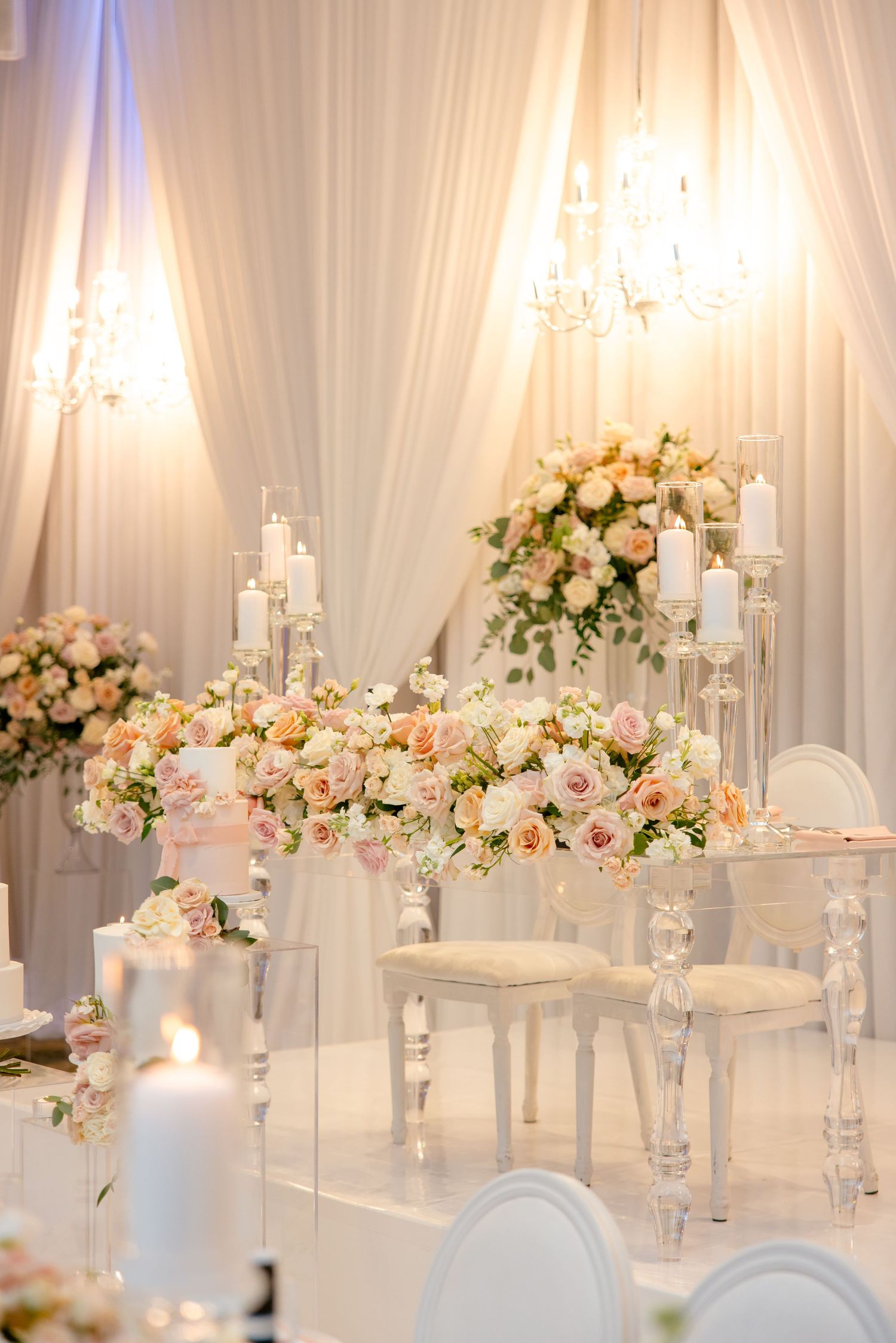 All-white wedding reception space with crystal chandeliers and romantic floral arrangements.
