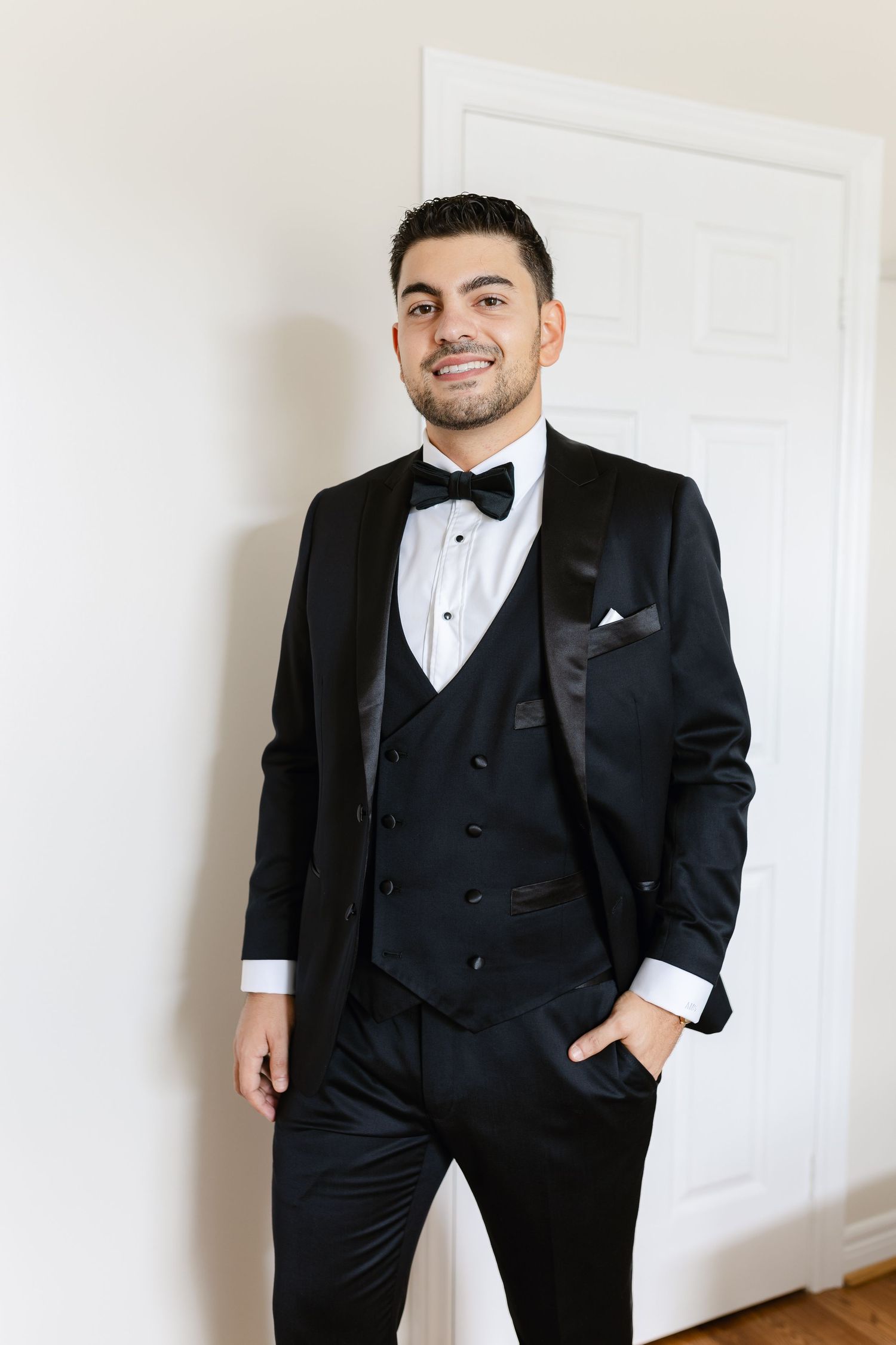 A classic black tuxedo with bow tie and vest photographed against a white wall.