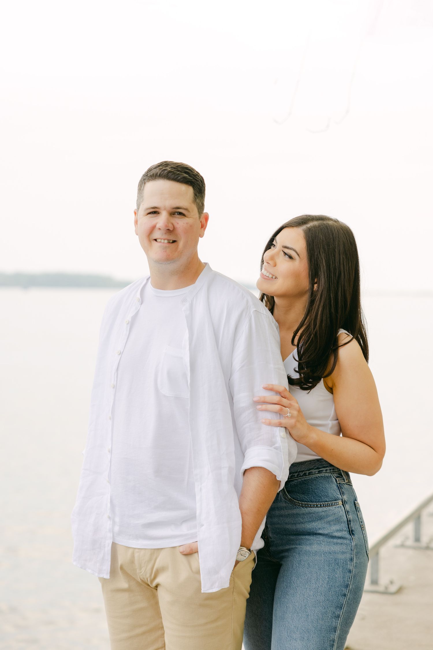 A couple shares a playful moment together by the waterfront on a bright day.