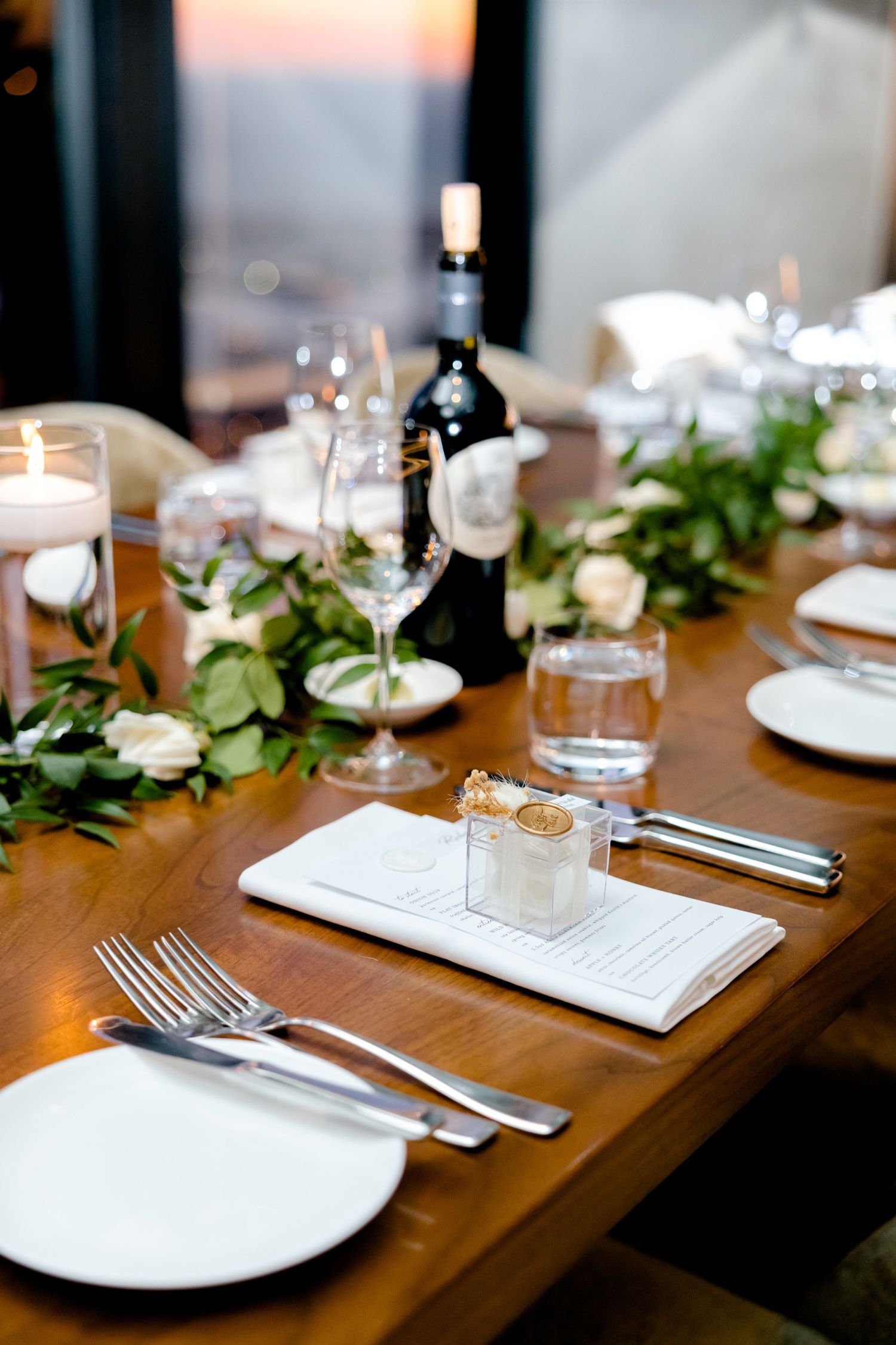 Elegant table setting with wine glasses, greenery garland, and candlelight for a wedding reception.