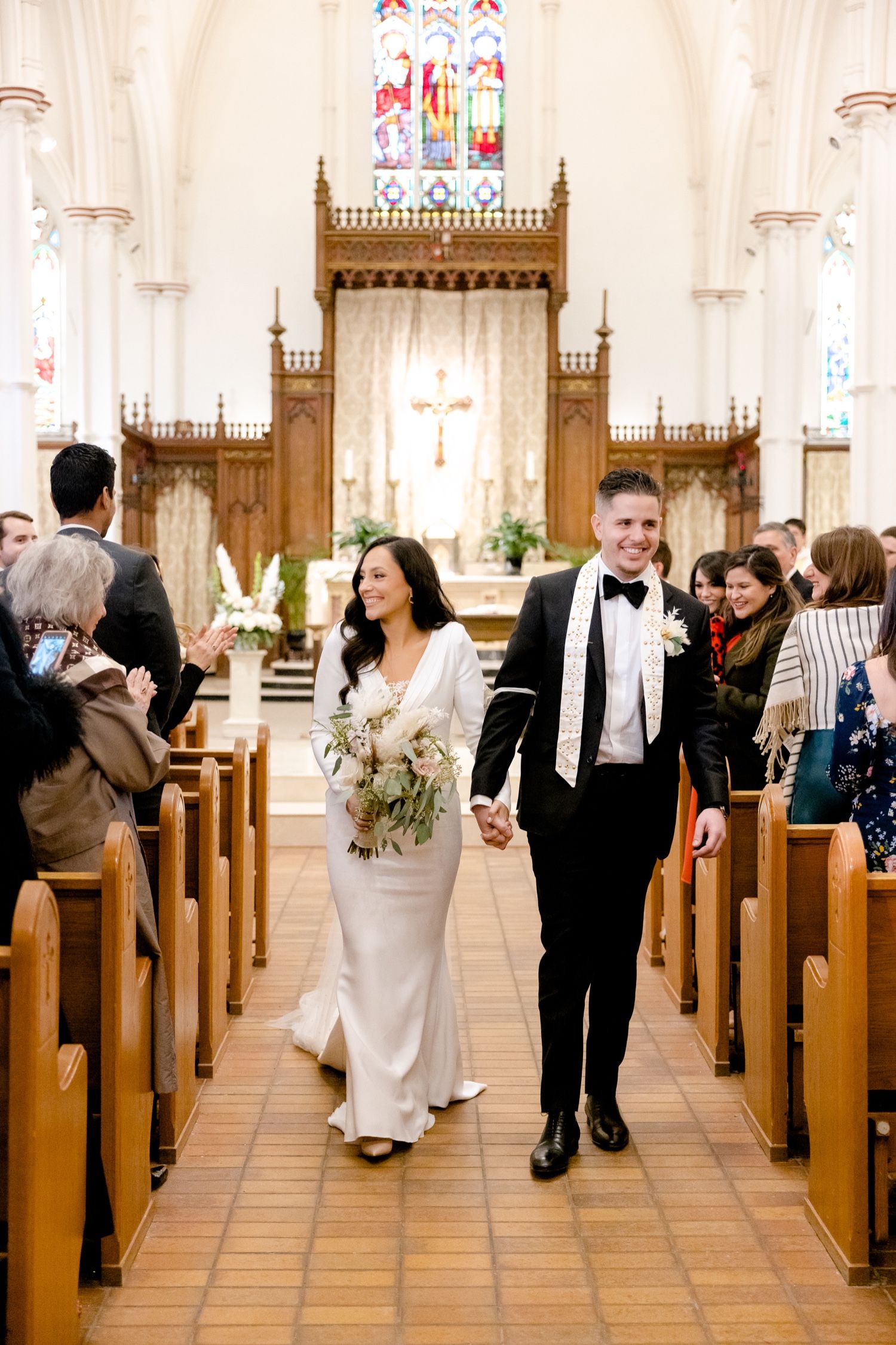 A wedding couple walking down the aisle of a church with guests seated in wooden pews.