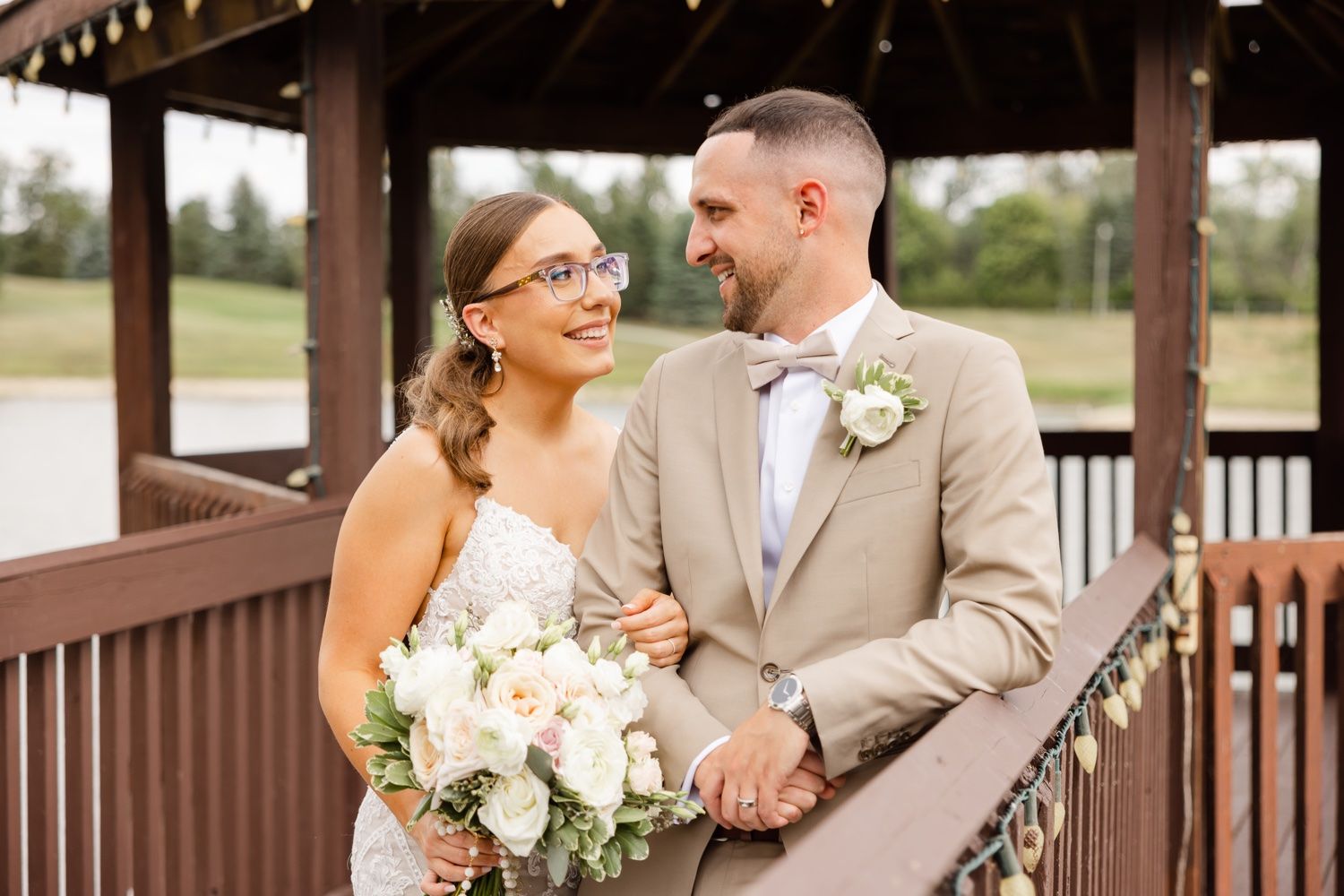 A couple shares an intimate moment on a wooden deck overlooking a lake during their wedding celebration.