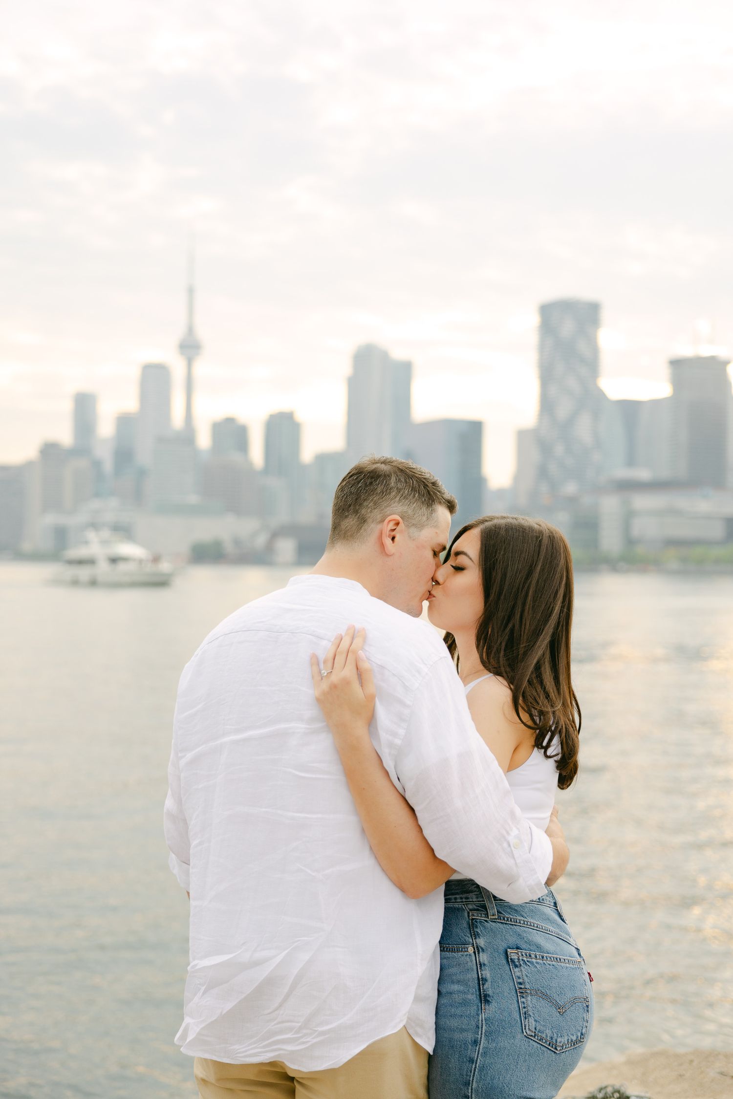 A romantic kiss captured on the shores of Lake Ontario with Toronto's skyline in view.