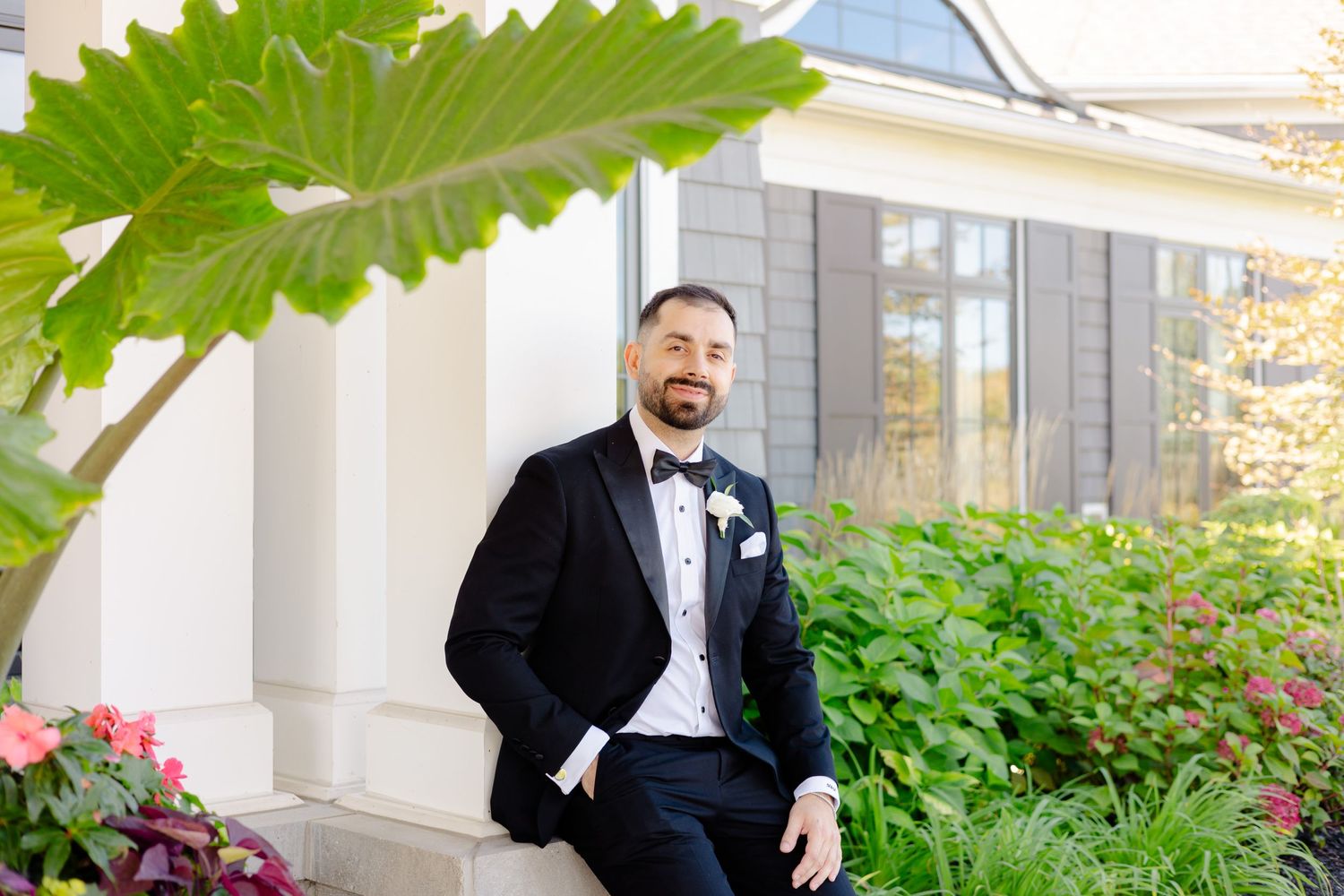 Elegant groom portrait under large green leaf with white architectural backdrop.