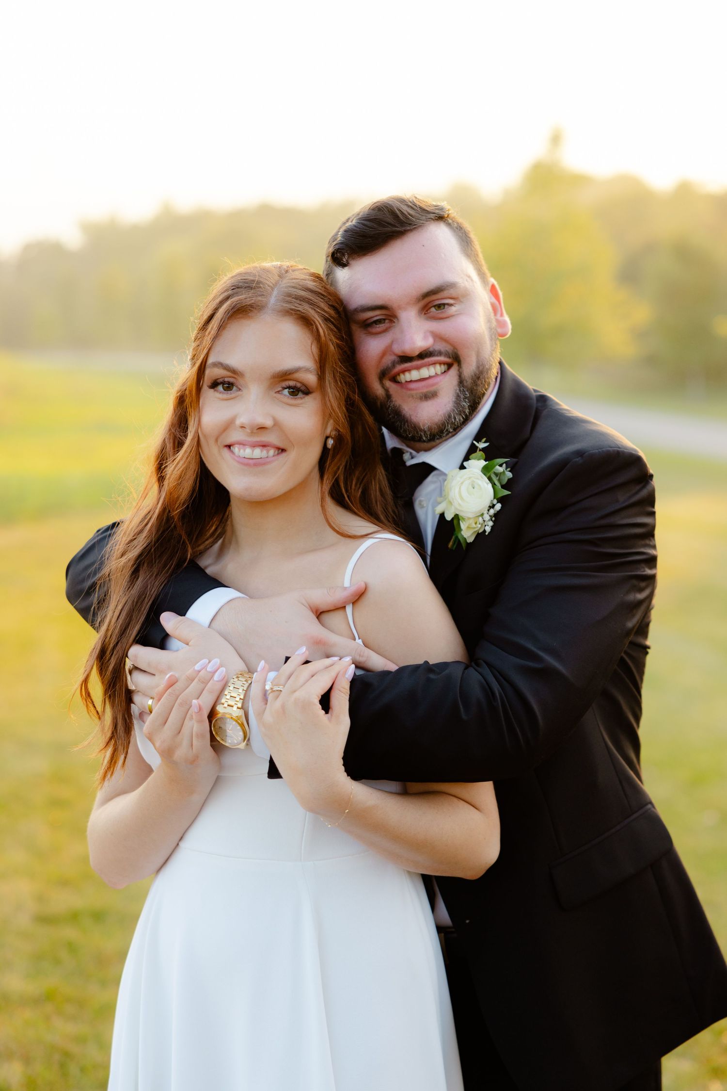 Happy wedding couple poses outdoors while embracing during golden hour photography.