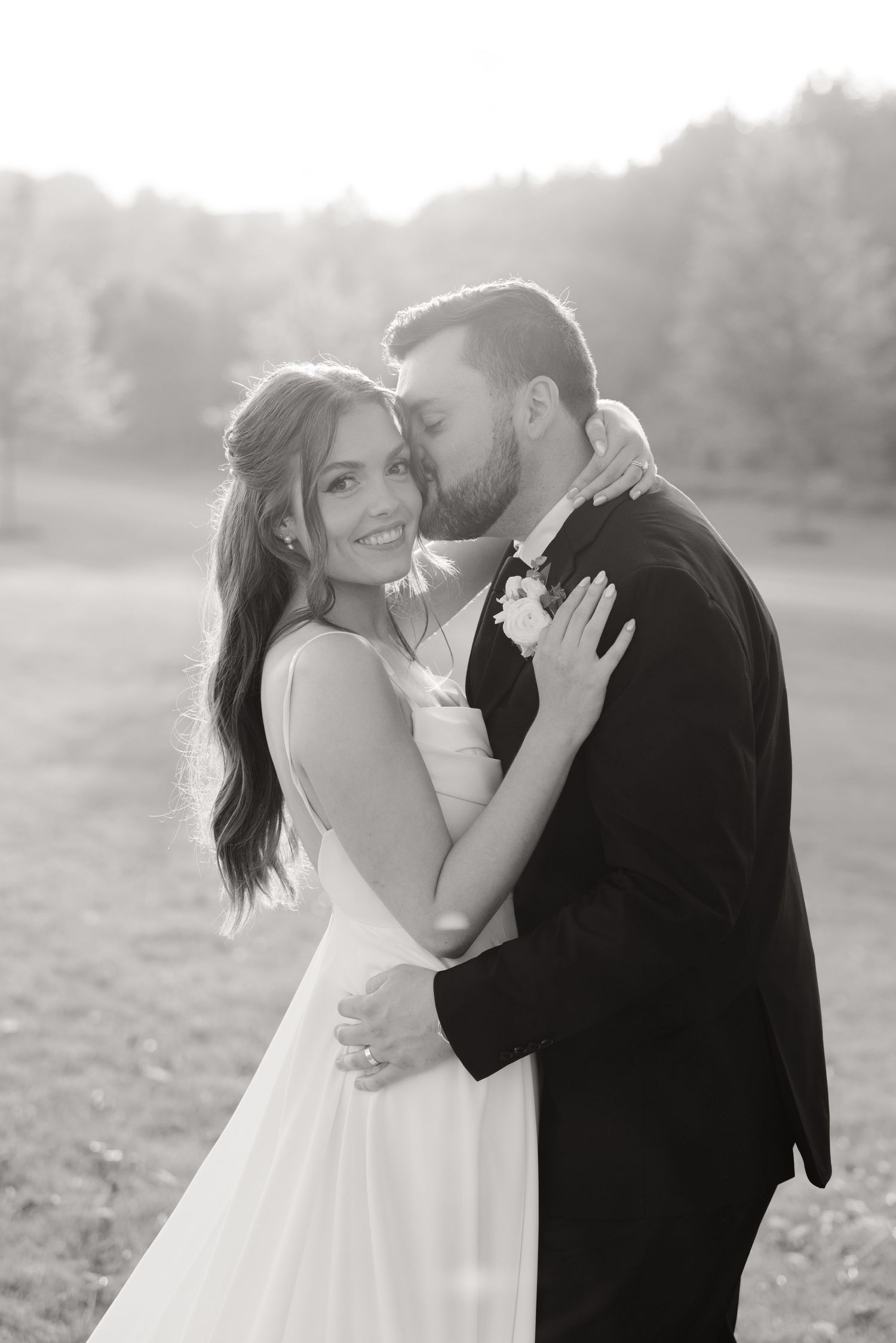 Black and white wedding portrait captures an intimate moment between newlyweds in a scenic field.
