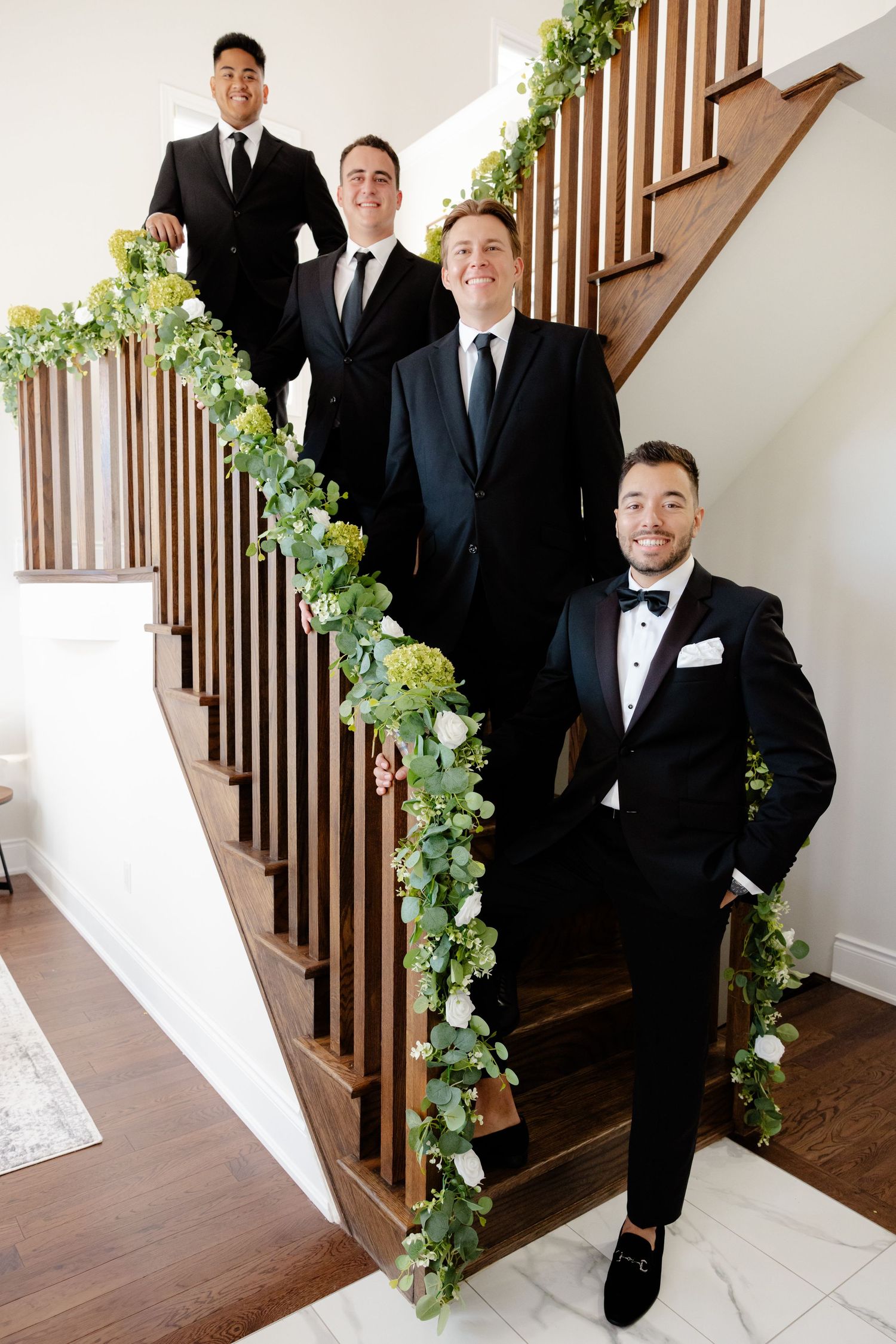 Wedding party members in dark suits stand positioned on flower-decorated staircase.