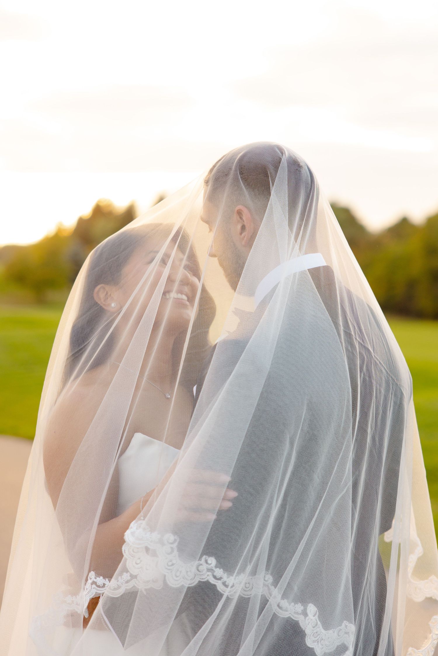 Romantic sunset wedding portrait with couple embracing beneath a translucent veil.