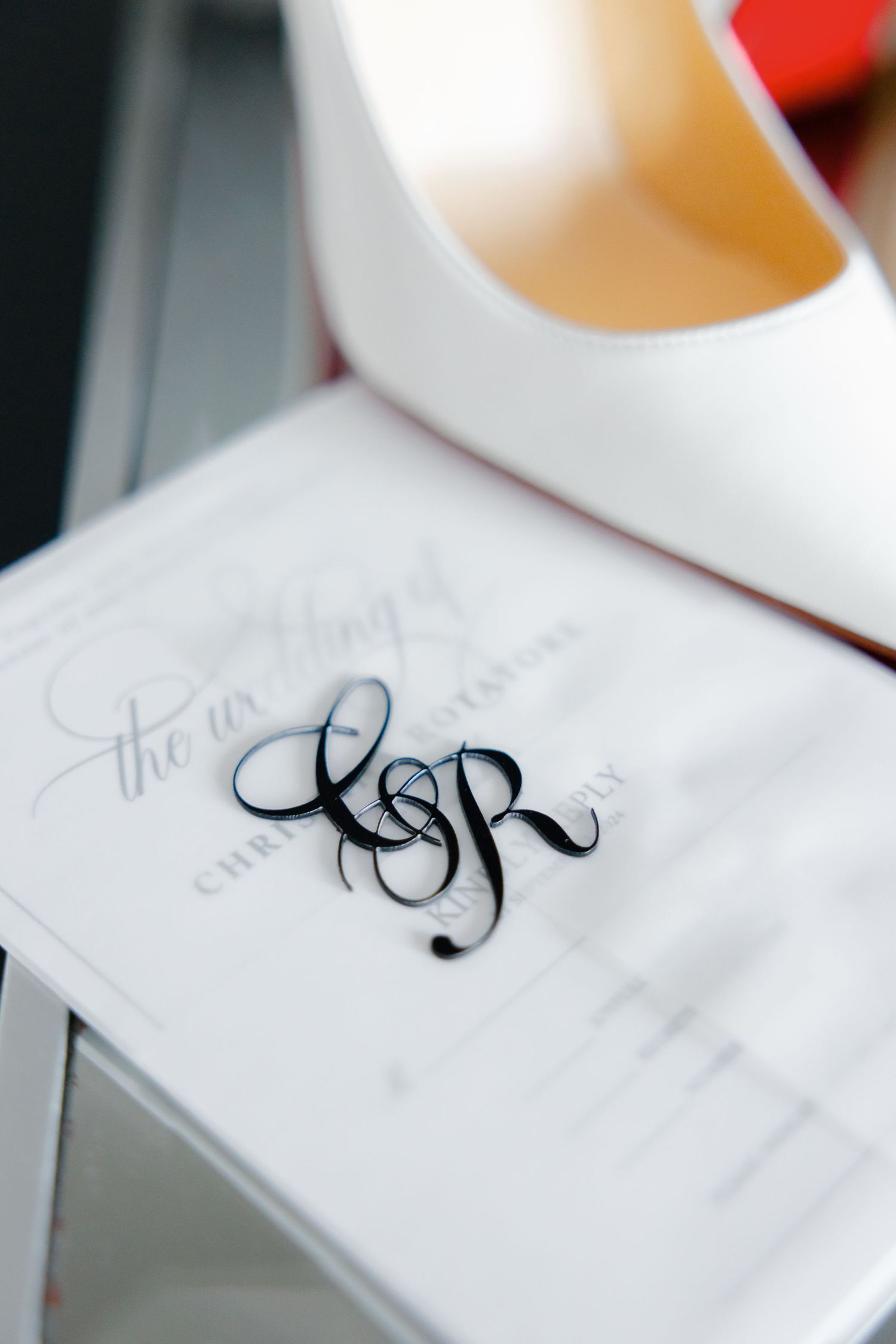 Close-up of monogrammed wedding stationery with initials SR next to white shoe.