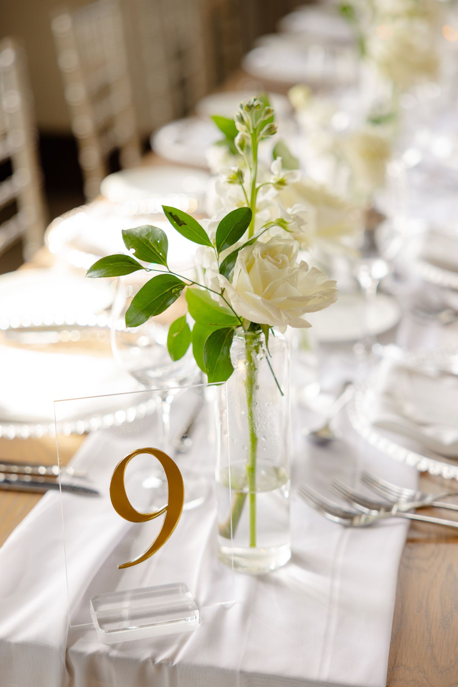 Elegant table setting with white rose centerpiece in clear vase and gold table number.