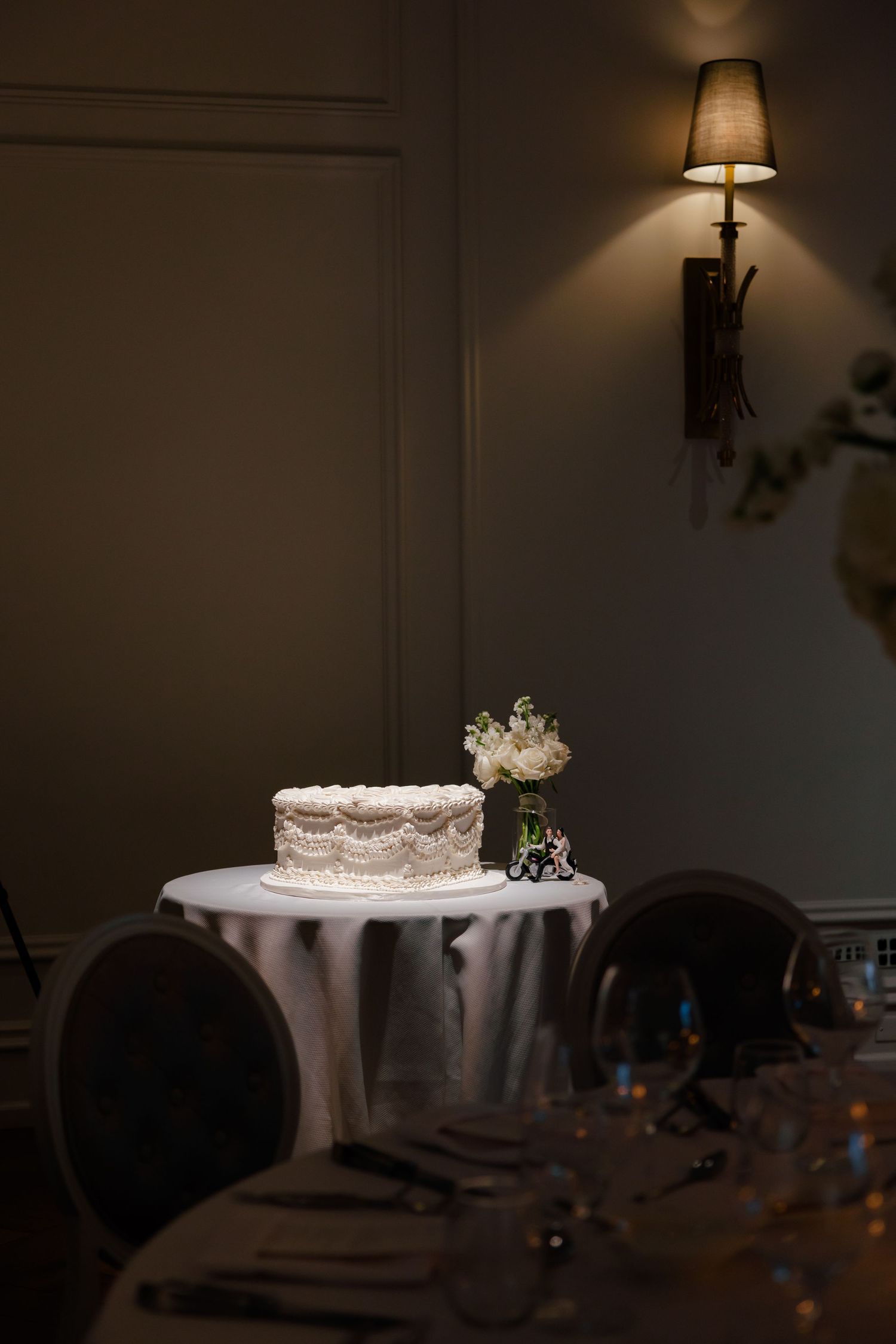 Wedding cake table setup with soft lamp lighting in romantic reception venue.