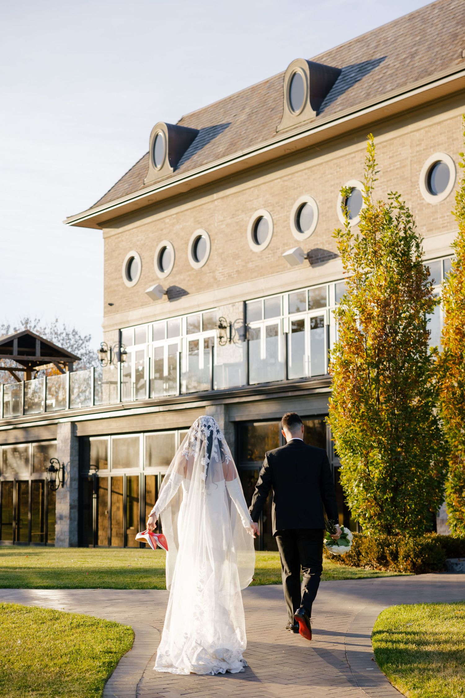 Wedding scene by elegant building with bride in flowing veil walking along landscaped path.