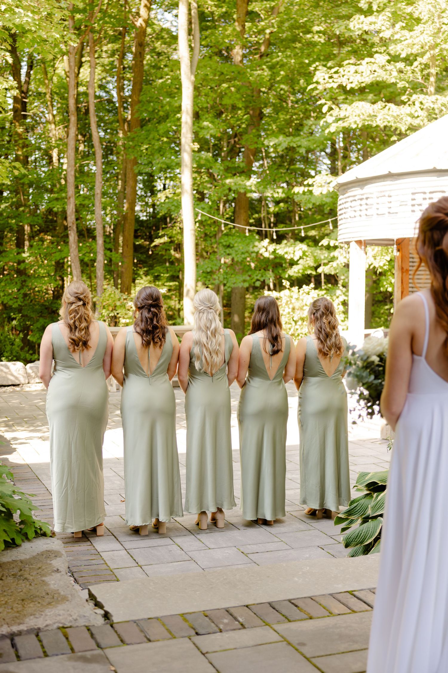 Bridesmaids in sage green dresses stand together showing their matching hairstyles.