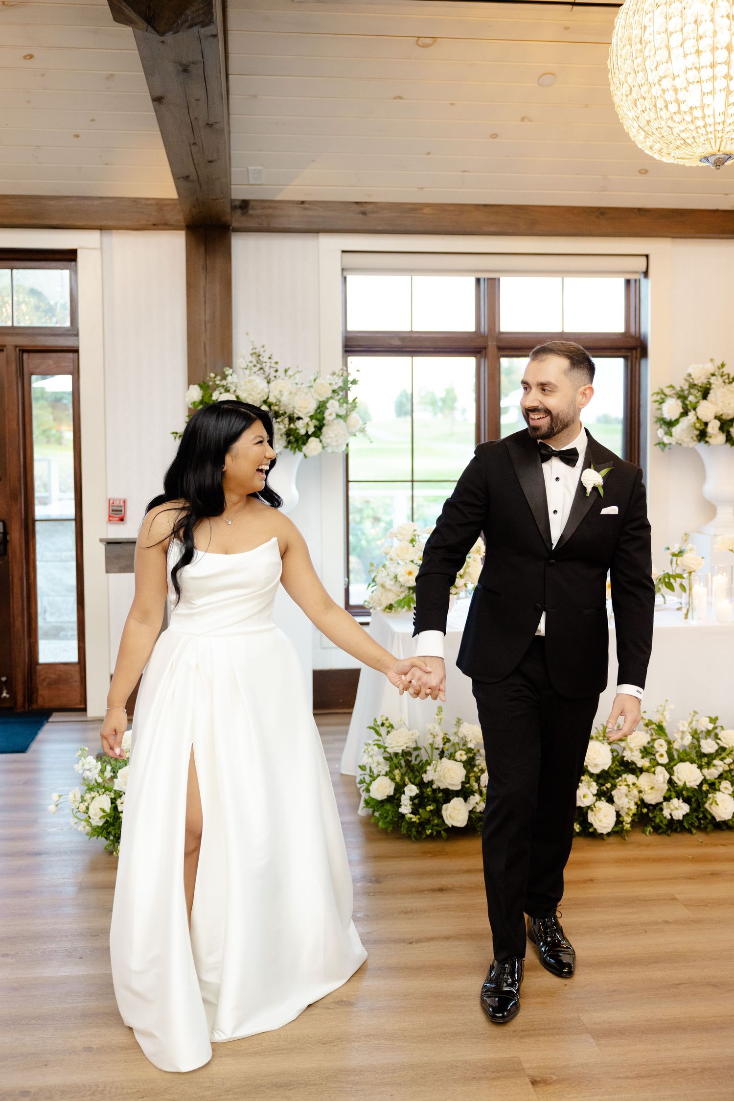 Elegant couple walks hand in hand in a reception venue decorated with floral arrangements.