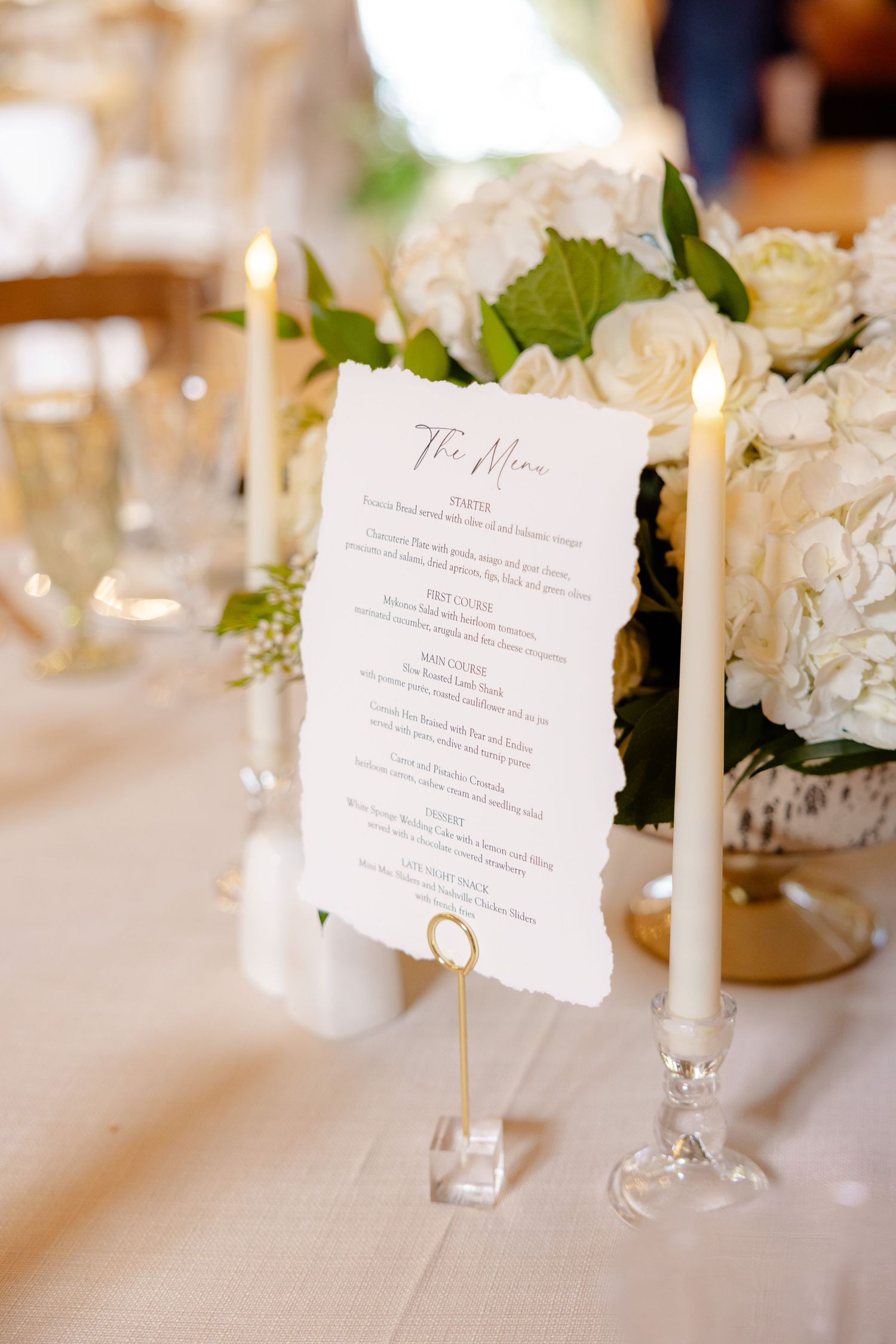 Wedding menu card displayed with white floral arrangements and champagne glasses.