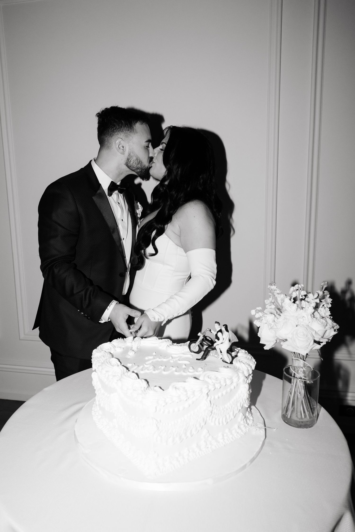 Black and white photo of newlyweds sharing an intimate moment by their wedding cake.