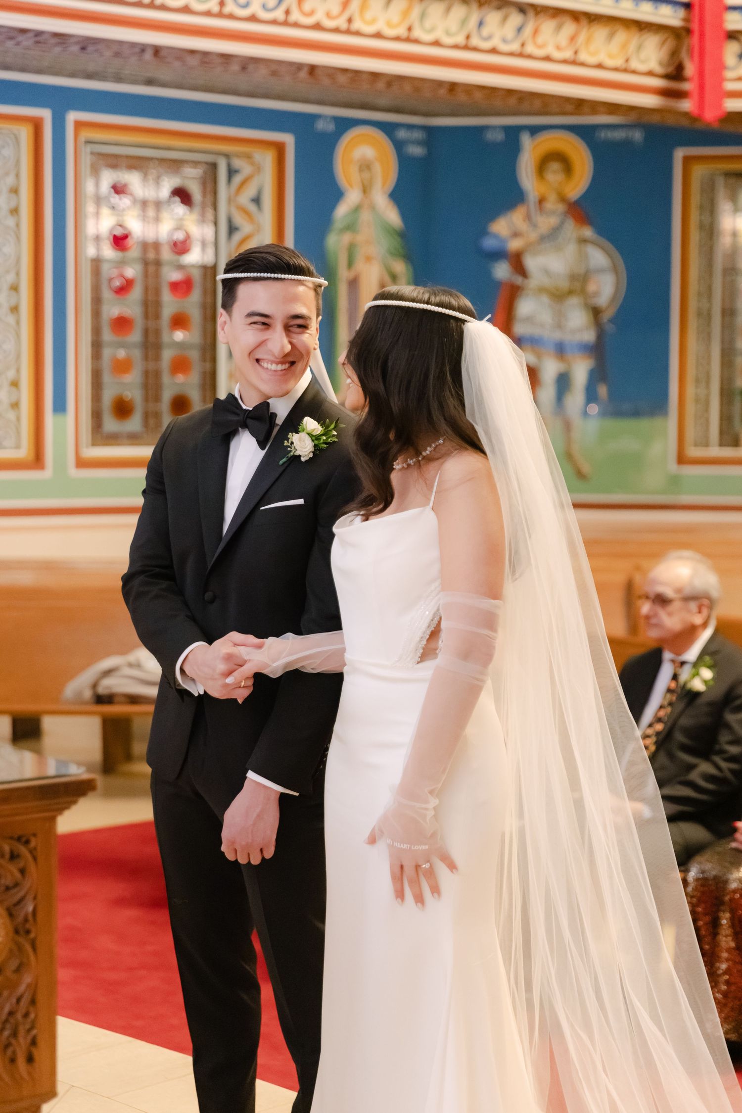 Newlyweds share a joyful moment in an ornate Orthodox church with religious icons in the background.