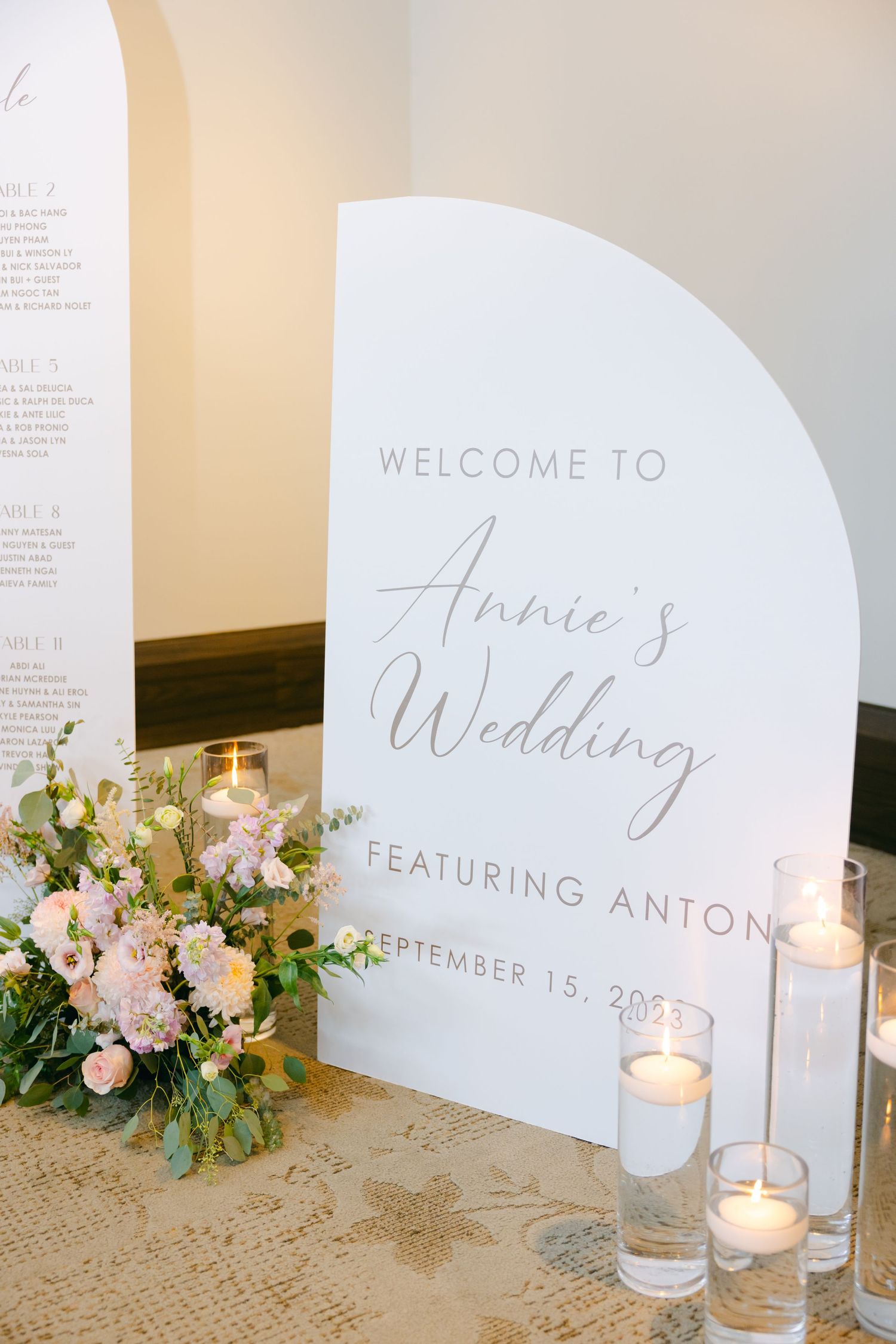 Modern wedding welcome sign with floral arrangements and candles in minimalist design.