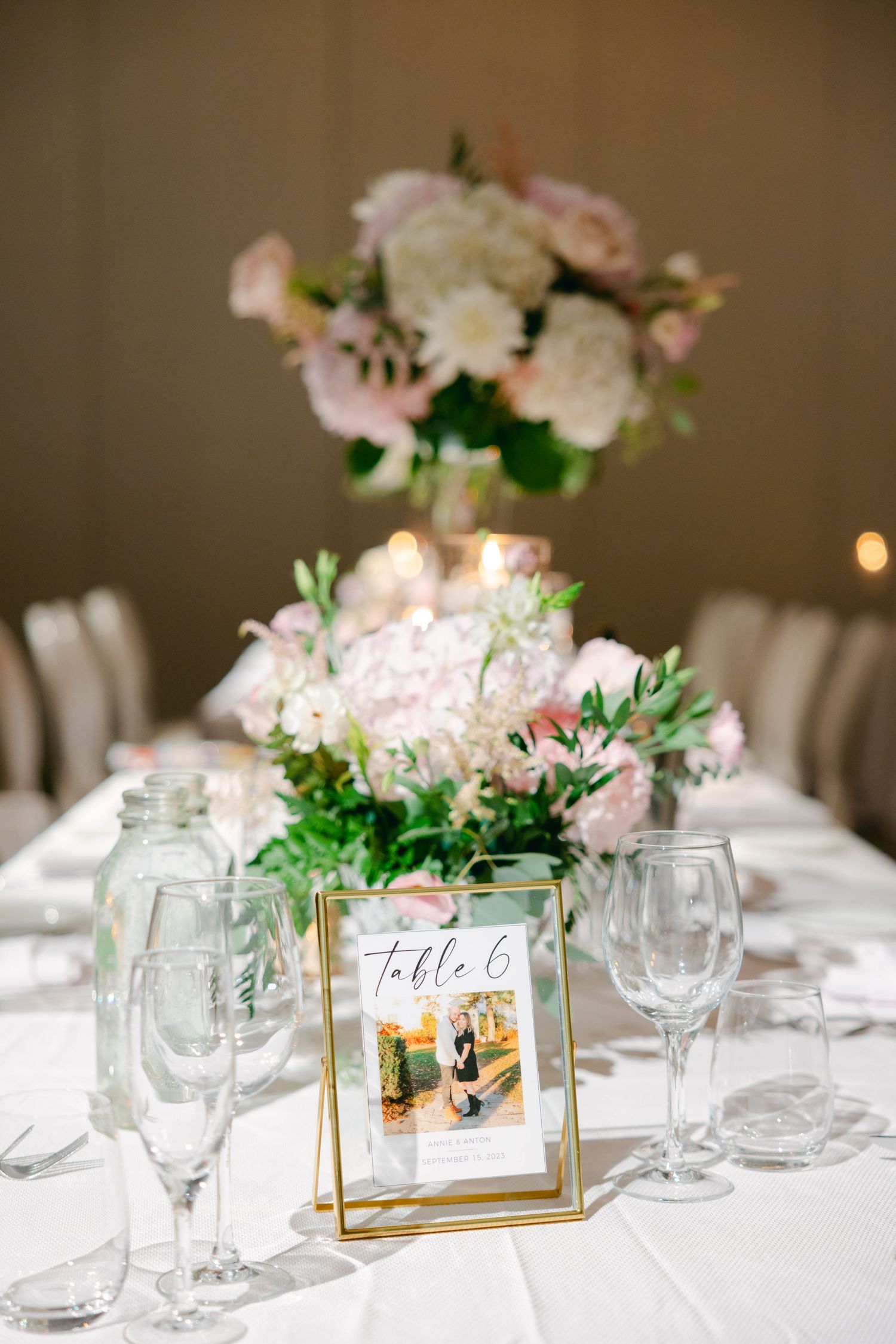 Elegant wedding table setting with framed table number and pink floral centerpiece on crisp white linens.