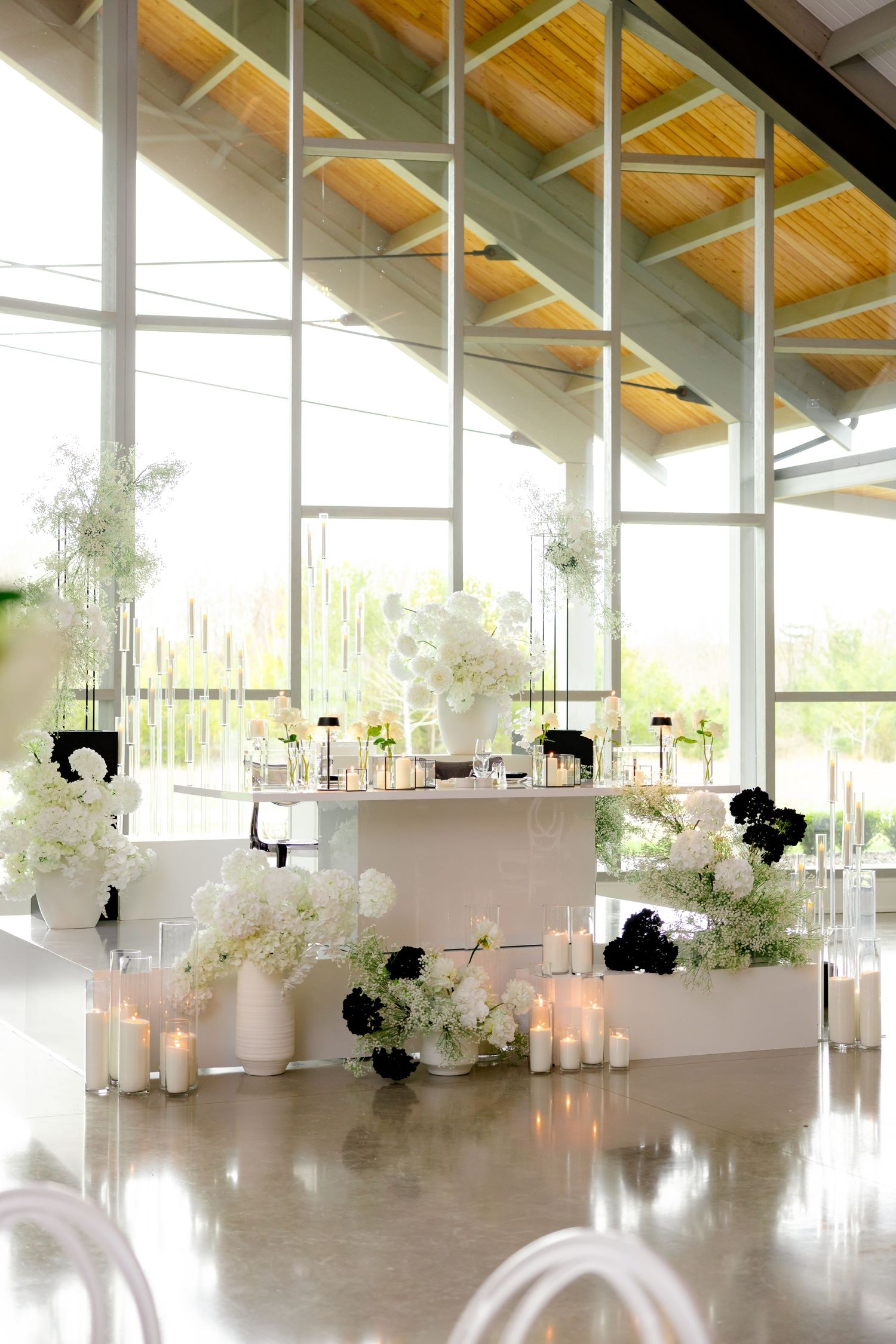 White tiered display with candles and floral arrangements in modern venue with large windows.
