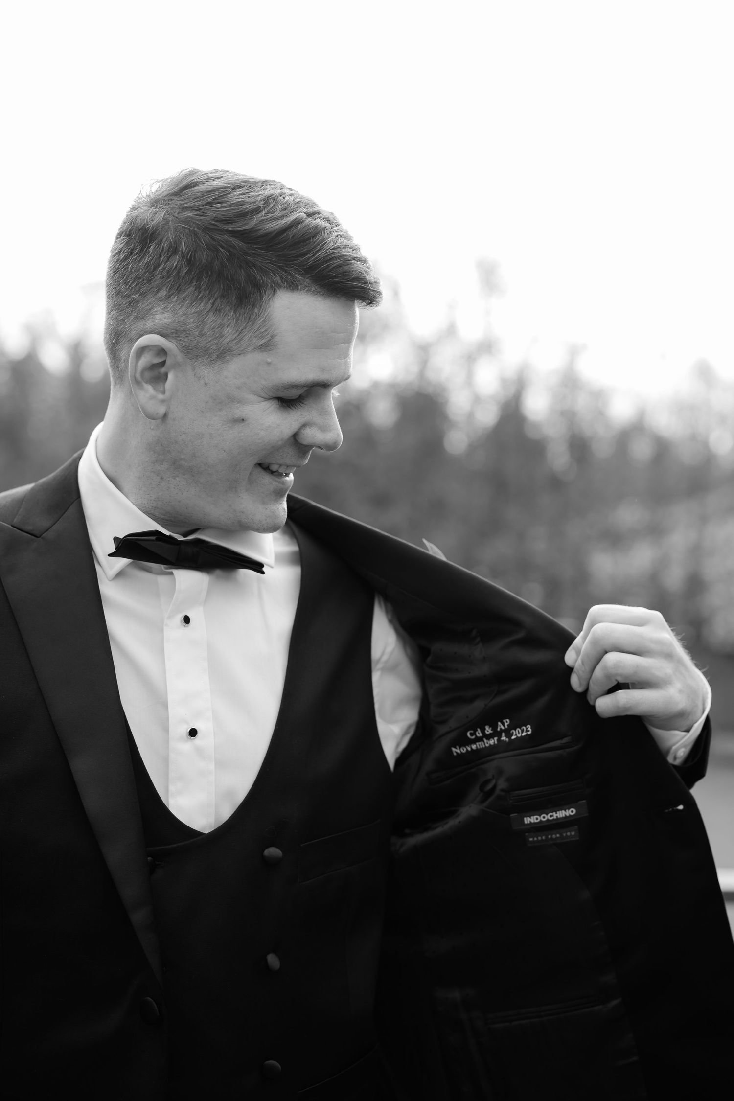 Black and white portrait of groom adjusting his tuxedo jacket.