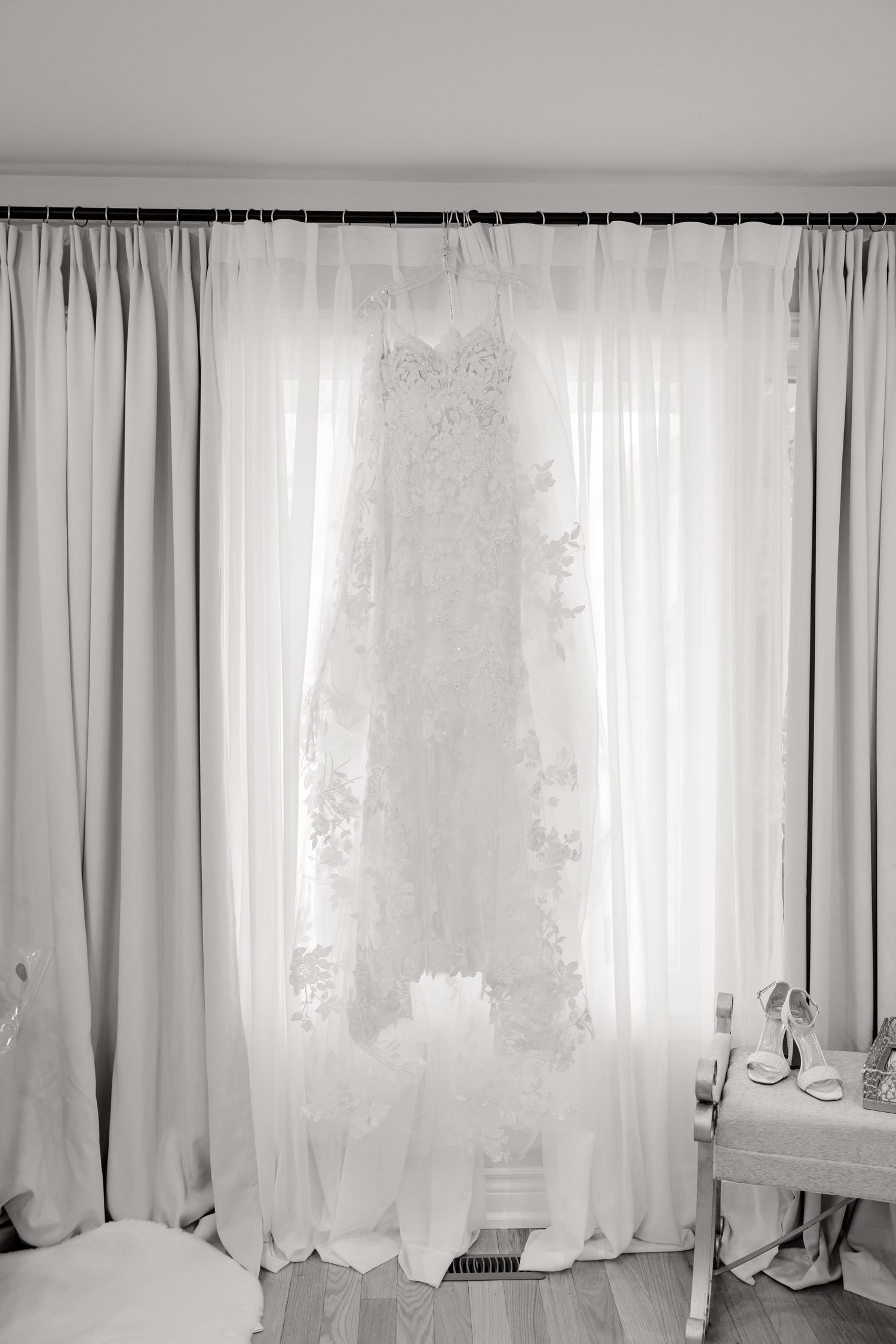 White wedding dress hanging in front of light curtains in a bridal preparation room.